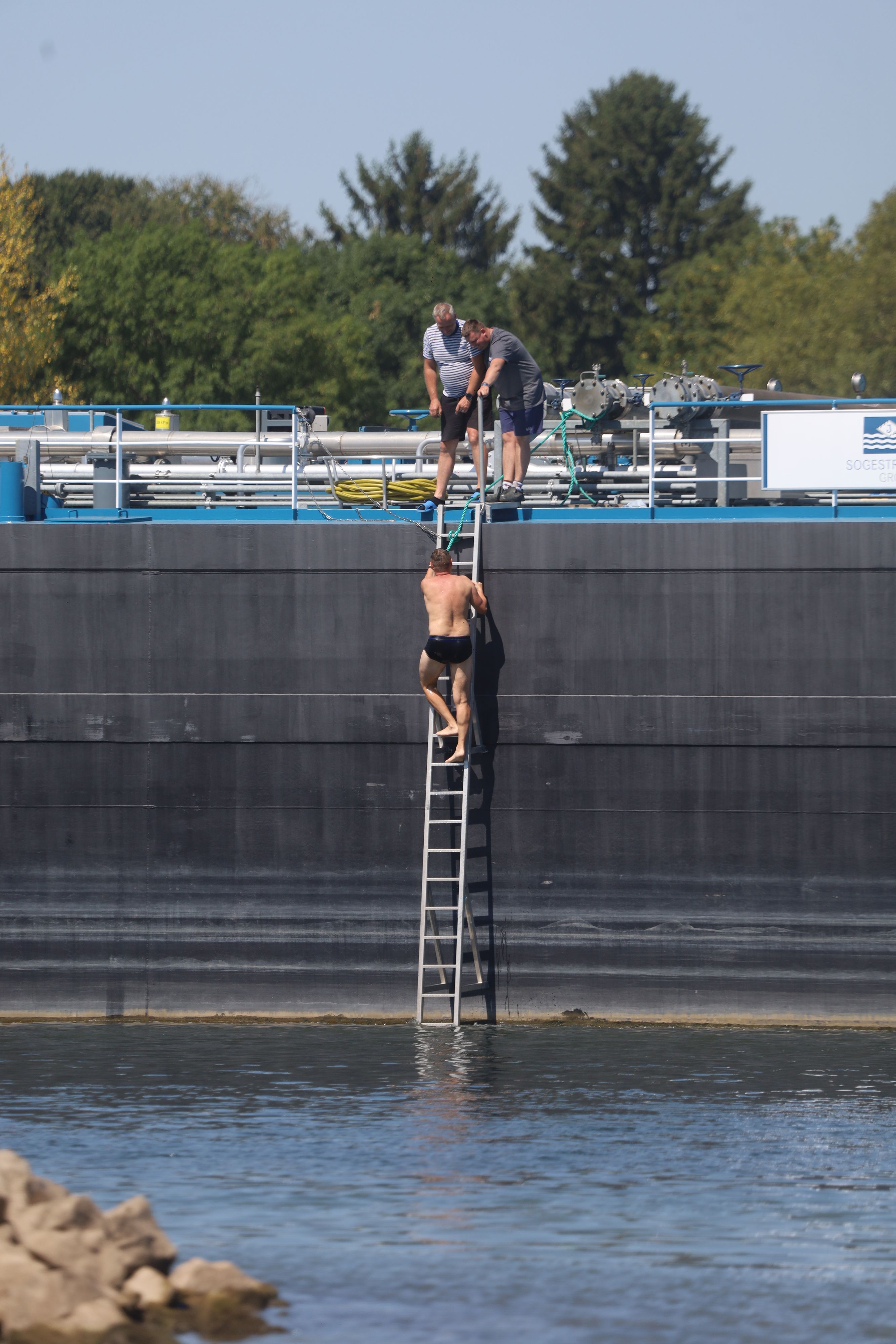 Ein Tankschiff liegt unweit des jachthafen in Zündorf im Rhein. Ein Mann in Badehose hat das Binnenschiff über eine Leiter verlassen und steht im Rhein. . Der Rhein führt extremes Niedrigwasser, immer neue Rekordwerte an den Pegeln beeinträchtigen auch die Schifffahrt.