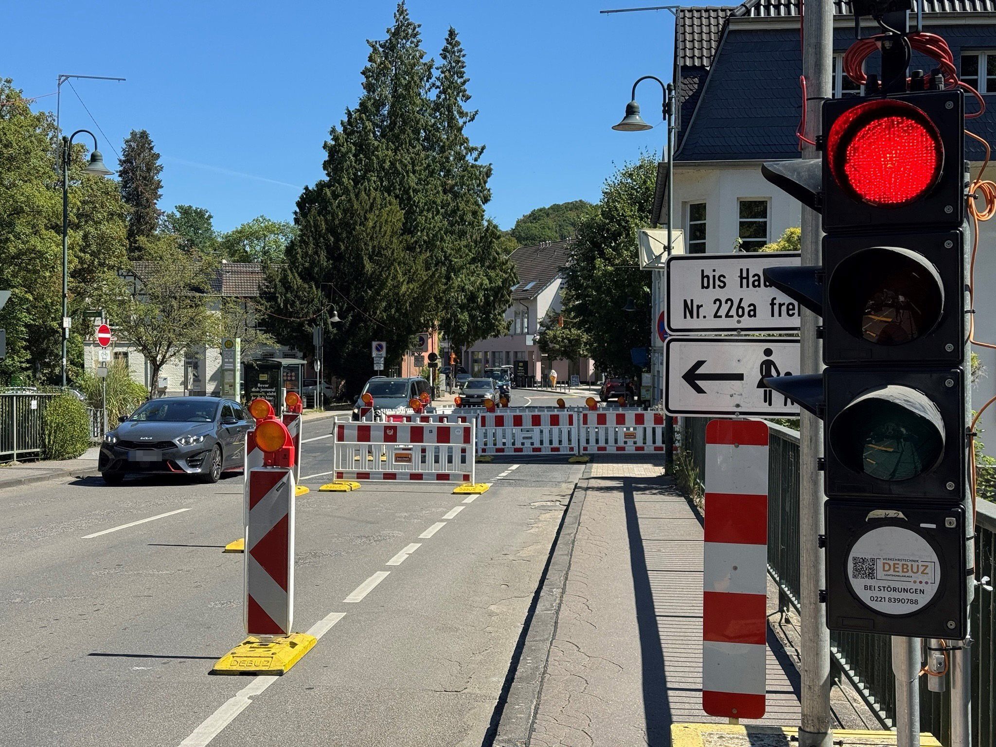 Eine Baustellenampel auf Rot und entgegenkommende Autos, etwas verdeckt  hinter einer Bake