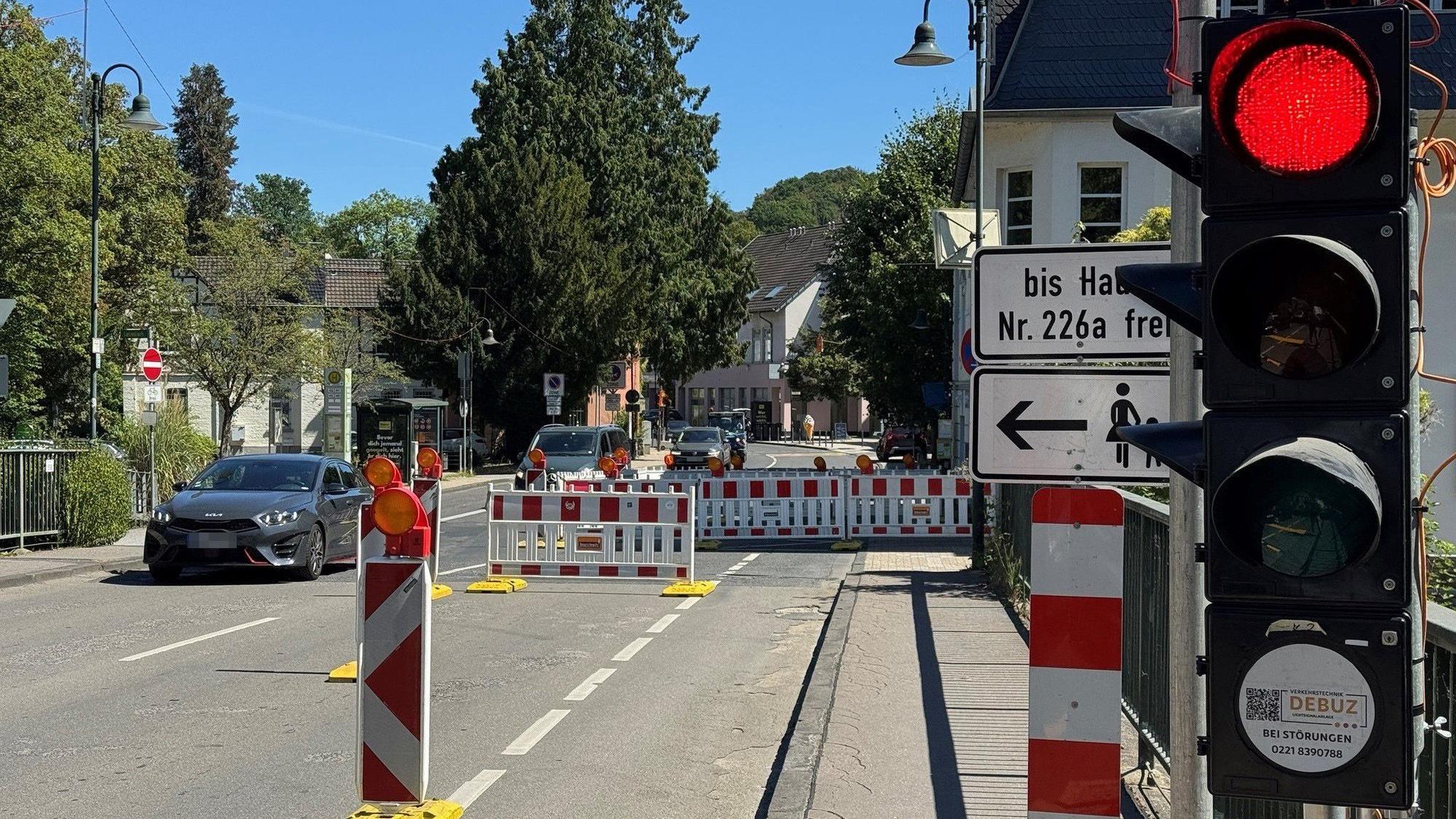 Eine Baustellenampel auf Rot und entgegenkommende Autos, etwas verdeckt hinter einer Bake