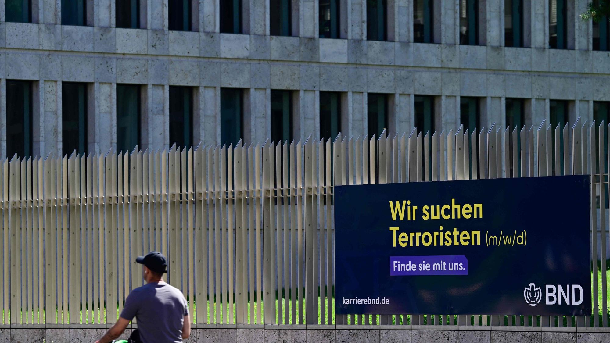 Ein Mann geht in Berlin an einer Stellenanzeige mit der Aufschrift „Wir suchen Terroristen“ vorbei, die am Zaun rund um die Zentrale des Bundesnachrichtendienstes (BND) angebracht ist. Die deutsche Regierung hat einer umfassenden Reform der Nachrichtendienste des Landes zugestimmt. Diese sollen weitreichende neue Befugnisse für verdeckte Operationen und Maßnahmen gegen Bedrohungen aus dem Ausland erhalten.