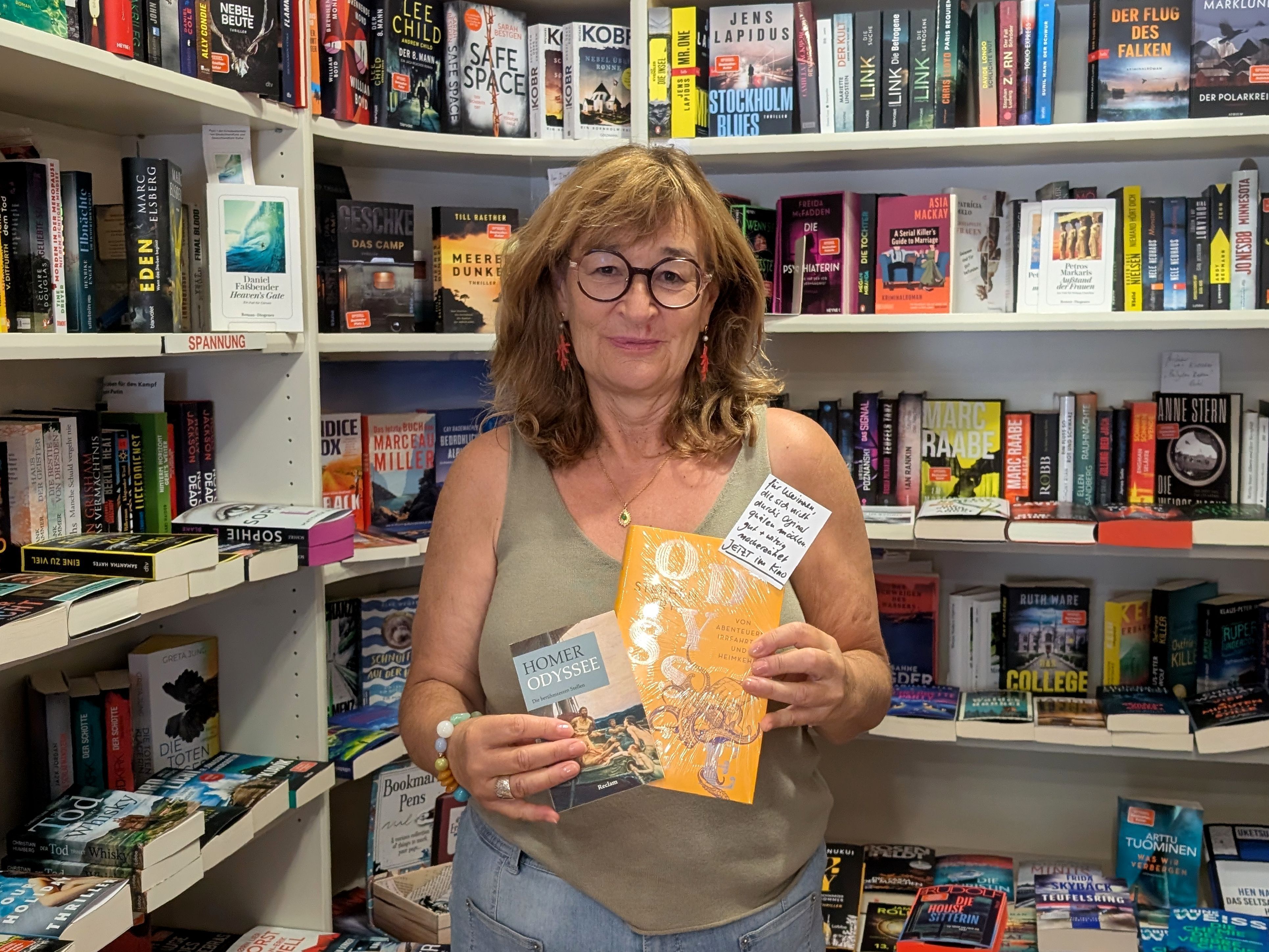 Buchhändlerin Renate Elsen steht mit zwei Büchern vor einem Regal.