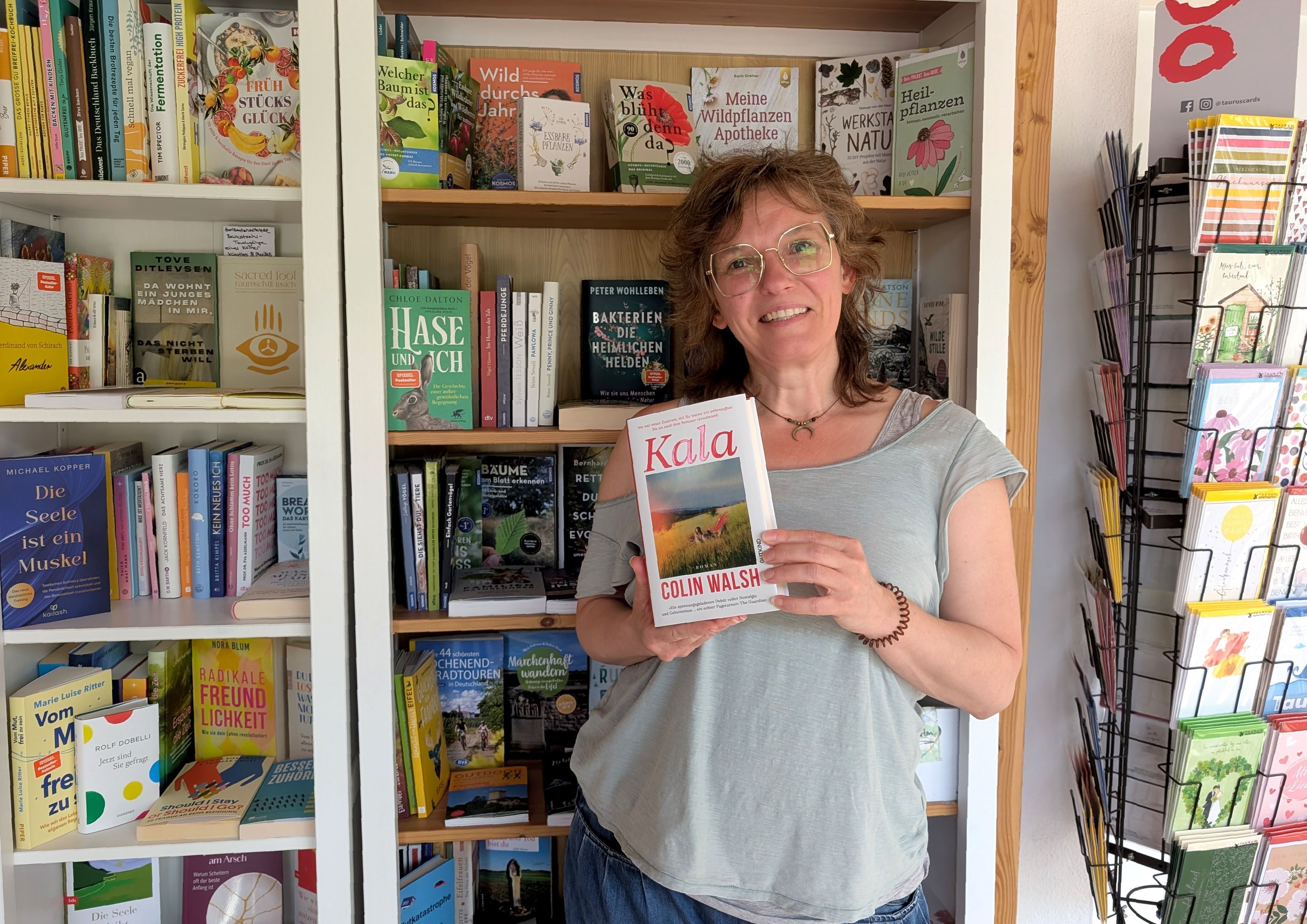 Buchhändlerin Rosa Wirtz  steht mit einem Buch vor einem Bücherregal.