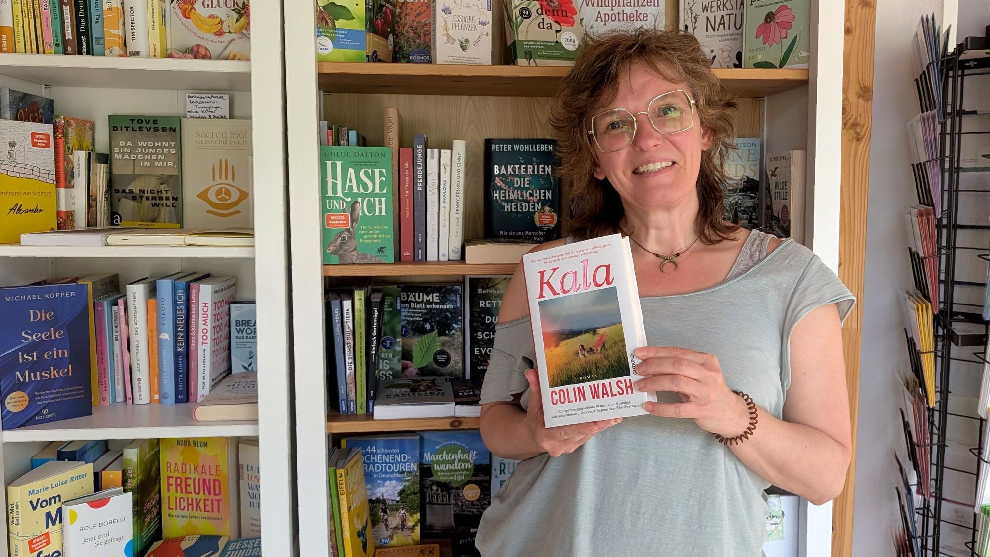 Buchhändlerin Rosa Wirtz steht mit einem Buch vor einem Bücherregal.