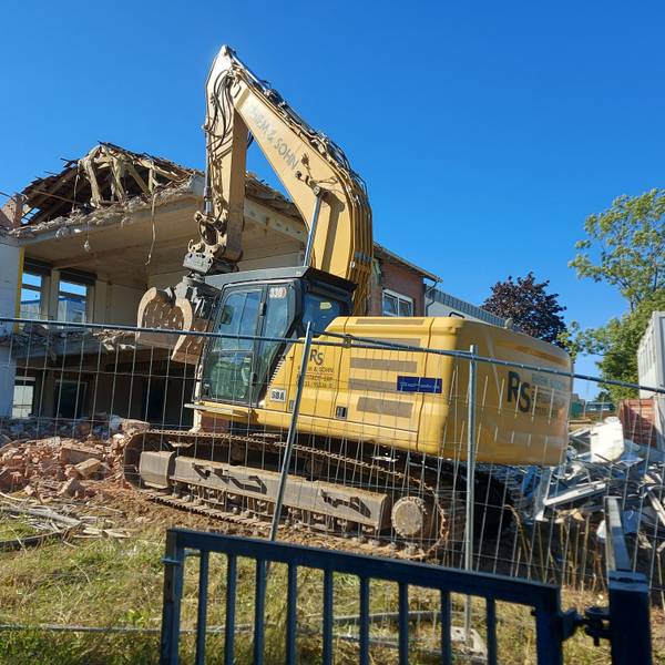 Ein gelber Bagger reißt die Wand eines Schulgebäudes ein.