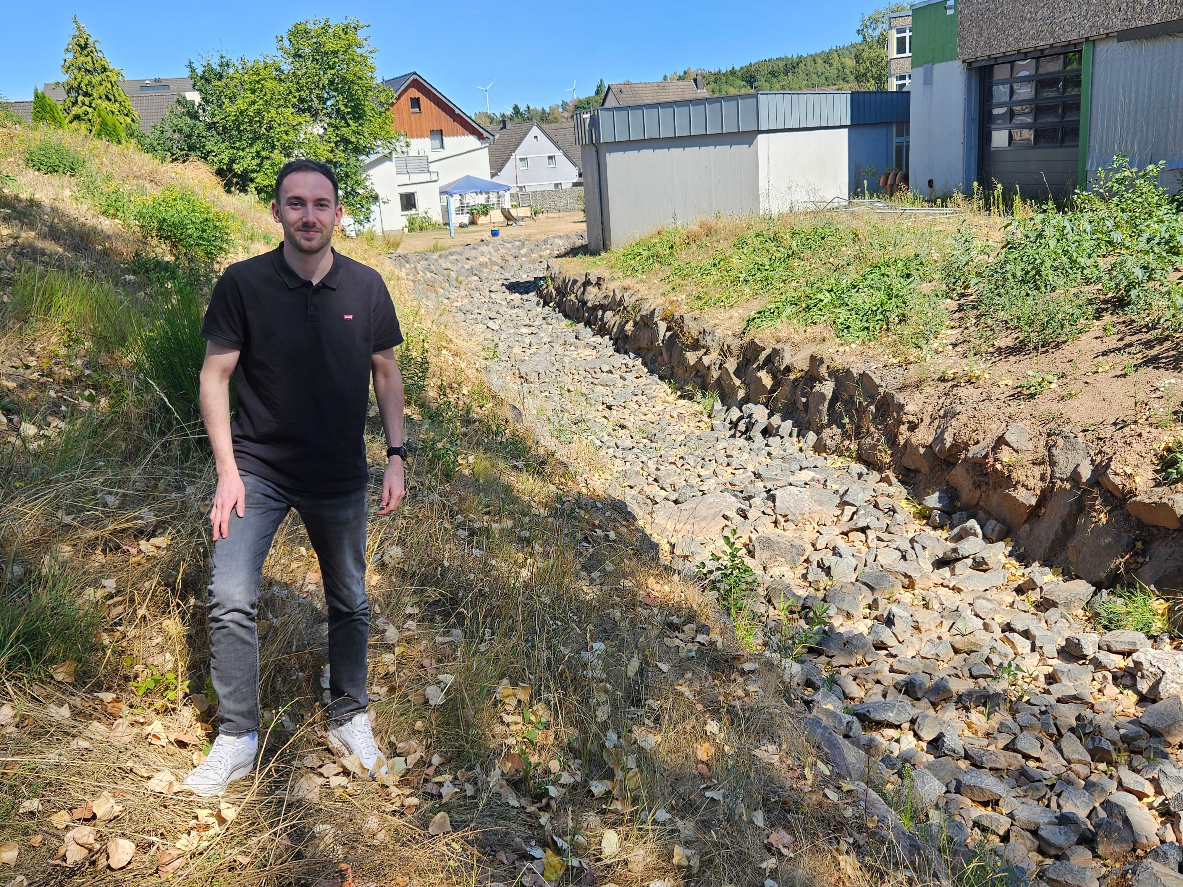 Ein junger Mann steht neben einem ausgetrockneten Bachbett.