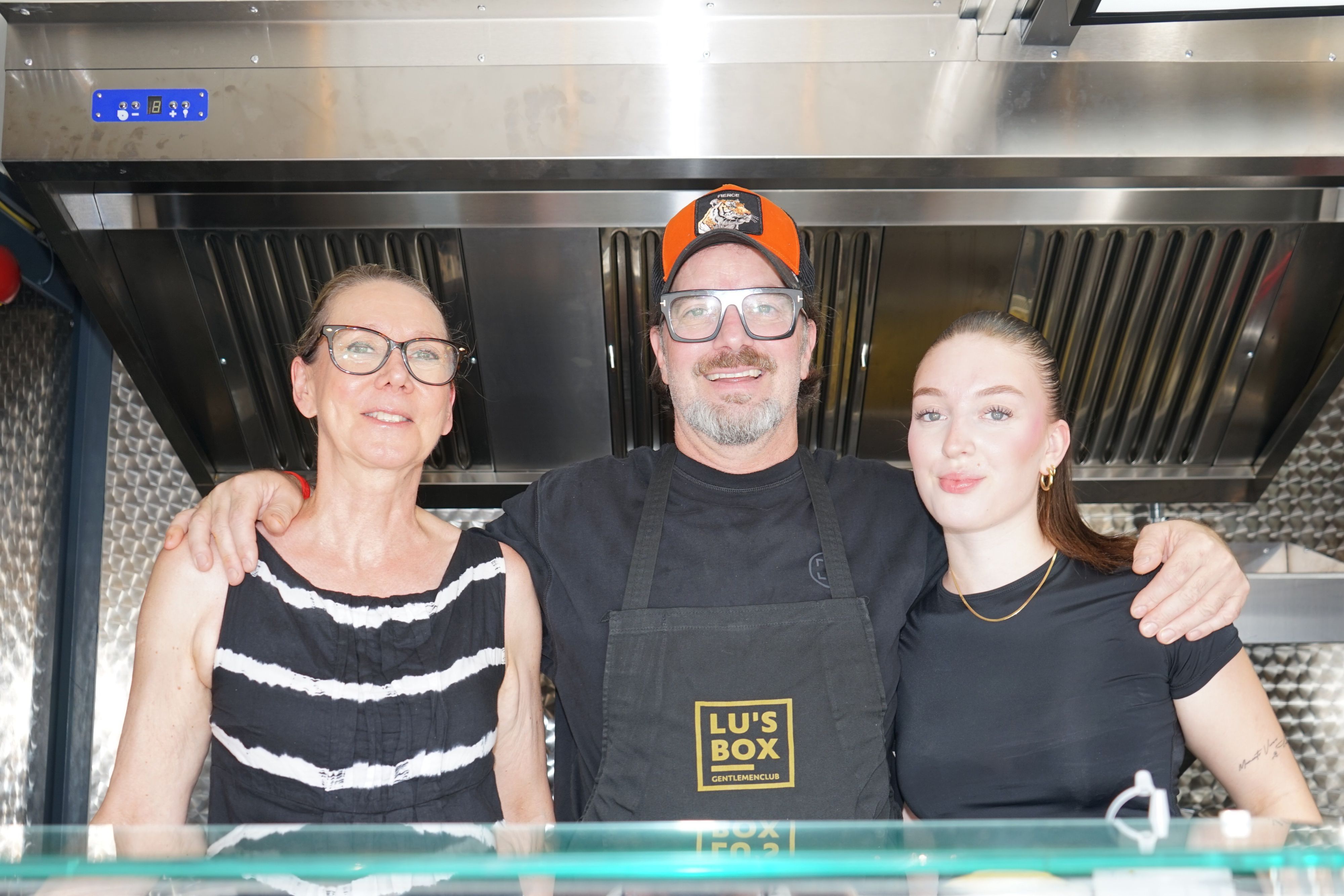 Zwei Frauen und ein Mann stehen in einem Foodtruck und lächeln in die Kamera.
