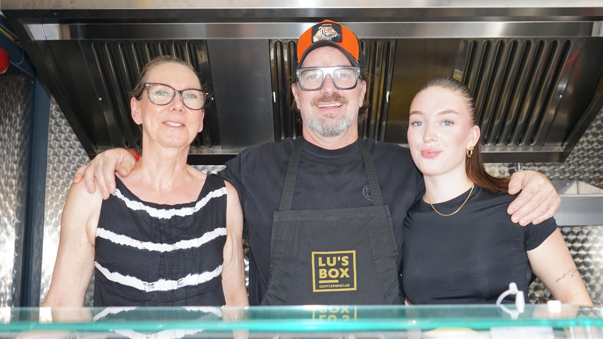 Zwei Frauen und ein Mann stehen in einem Foodtruck und lächeln in die Kamera.