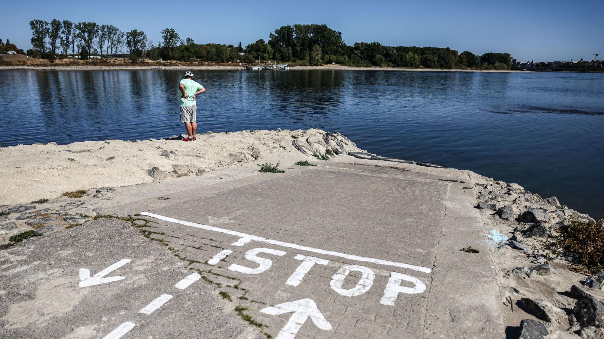 Ein Mann steht am Anleger einer Personenfähre bei Niedrigwasser am Kölner Rheinufer. Das Wetter bleibt zunächst trocken und heiß.