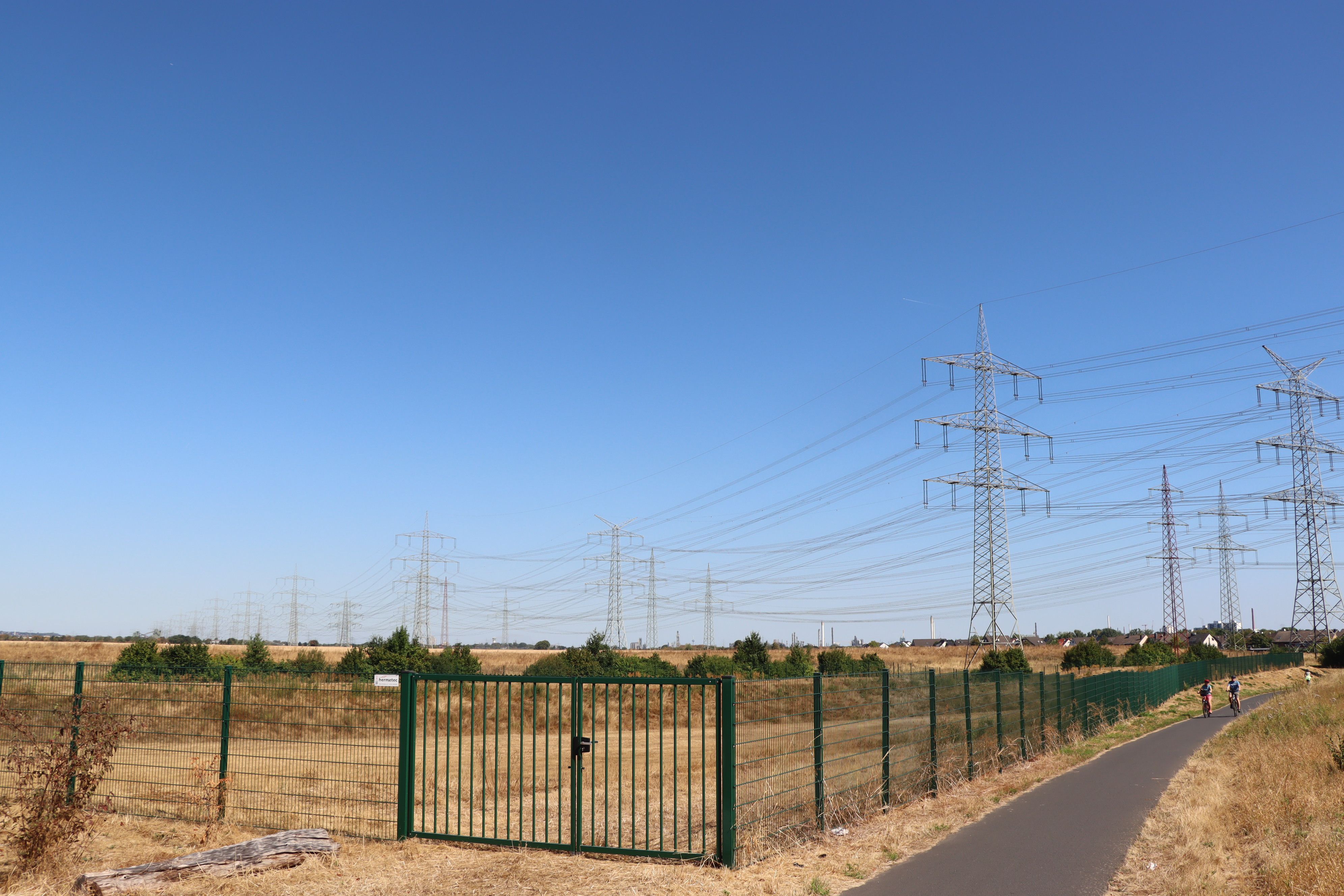 Das Bild zeigt ein eingezäuntes Areal, dahinter sind blauer Himmel und Freileitungen zu sehen.