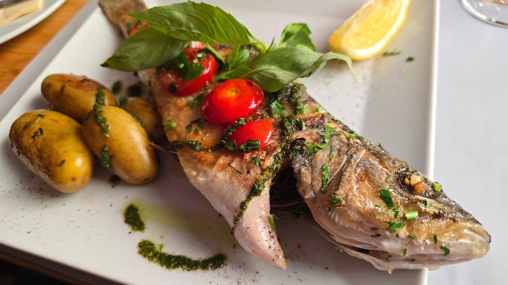 Fisch garniert mit Pesto, Tomaten und Basilikum. Anbei Kartoffeln.