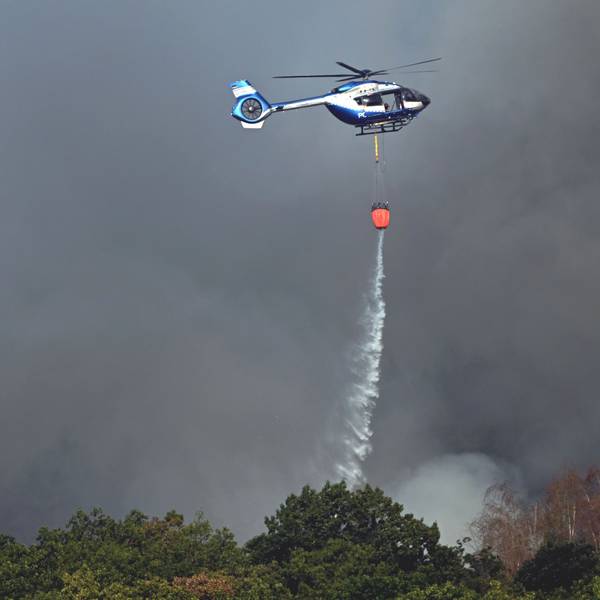 Ein Polizeihubschrauber mit Löschwasser-Außenlastbehälter unterstützt die Löscharbeiten beim Waldbrand im Hürtgenwald.