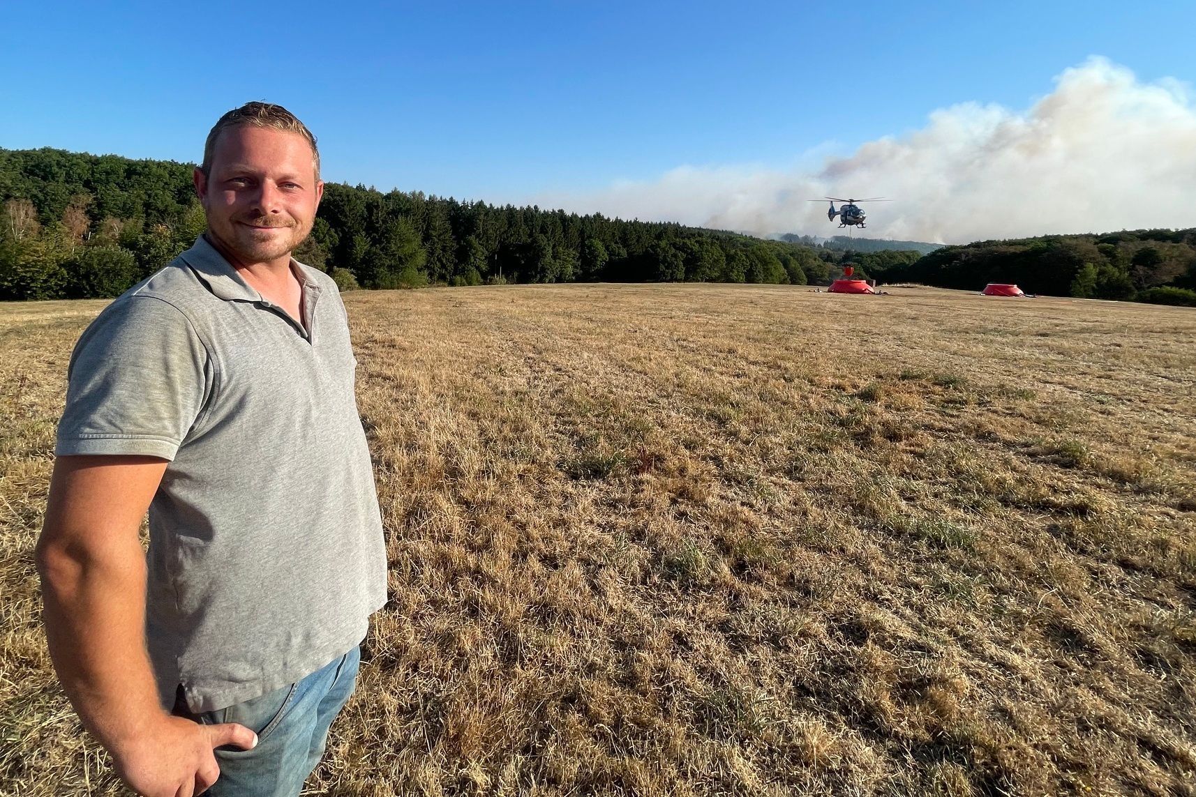 Patrick Koch, der die Feuerwehr beim Waldbrand im Hürtgenwald die ganze Nacht über mit einem Traktor mit Wasser aus einer Talsperre beliefert hat, steht auf einem Feld unweit des Waldbrandes.
