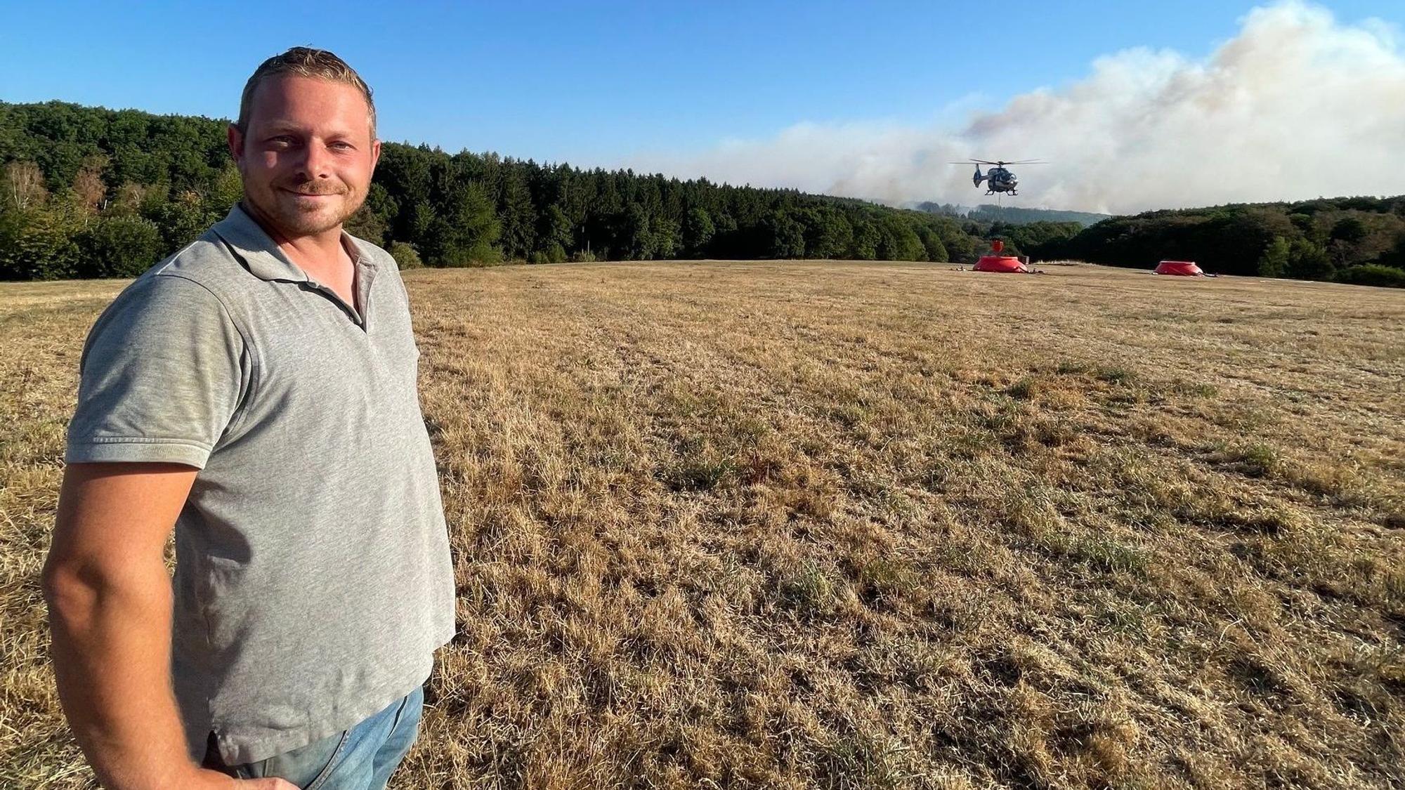 Patrick Koch, der die Feuerwehr beim Waldbrand im Hürtgenwald die ganze Nacht über mit einem Traktor mit Wasser aus einer Talsperre beliefert hat, steht auf einem Feld unweit des Waldbrandes.