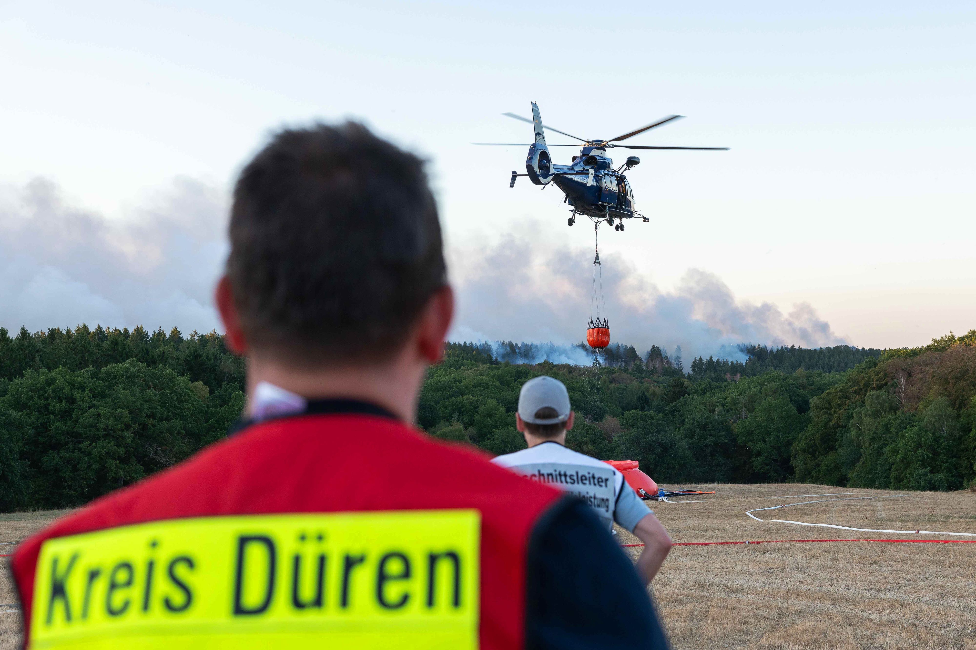 13.08.2026, Nordrhein-Westfalen, Hürtgenwald: Ein Löschhubschrauber ist bei einem Waldbrand im Hürtgenwald im Einsatz. Wegen des Waldbrandes in der Gemeinde Hürtgenwald wird der Ortsteil Gey evakuiert. Foto: Jan Ohmen/dpa +++ dpa-Bildfunk +++