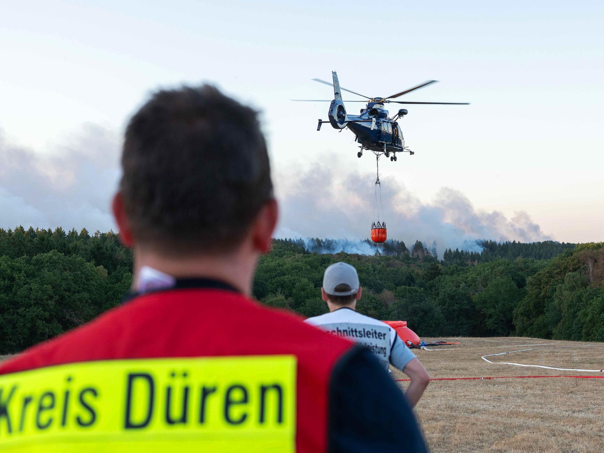 13.08.2026, Nordrhein-Westfalen, Hürtgenwald: Ein Löschhubschrauber ist bei einem Waldbrand im Hürtgenwald im Einsatz. Wegen des Waldbrandes in der Gemeinde Hürtgenwald wird der Ortsteil Gey evakuiert. Foto: Jan Ohmen/dpa +++ dpa-Bildfunk +++