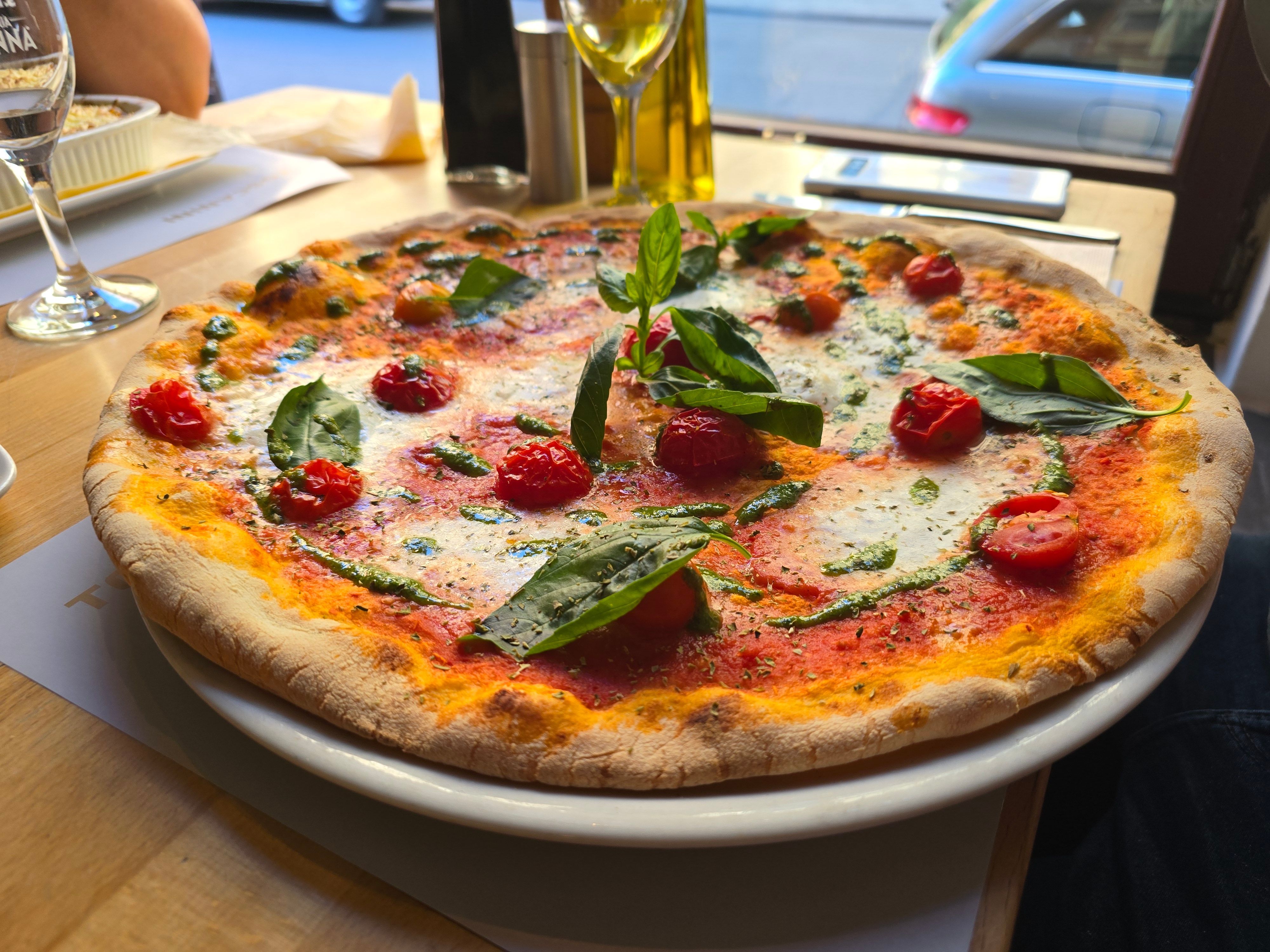 Pizza belegt mit Tomaten und Basilikum, grünem Pesto und Mozzarella, liegt auf einem Teller.