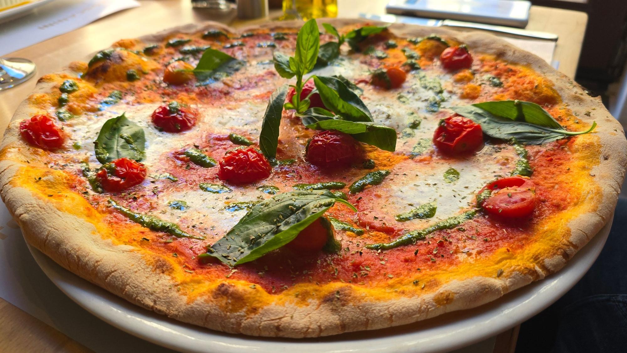 Pizza belegt mit Tomaten und Basilikum, grünem Pesto und Mozzarella, liegt auf einem Teller.