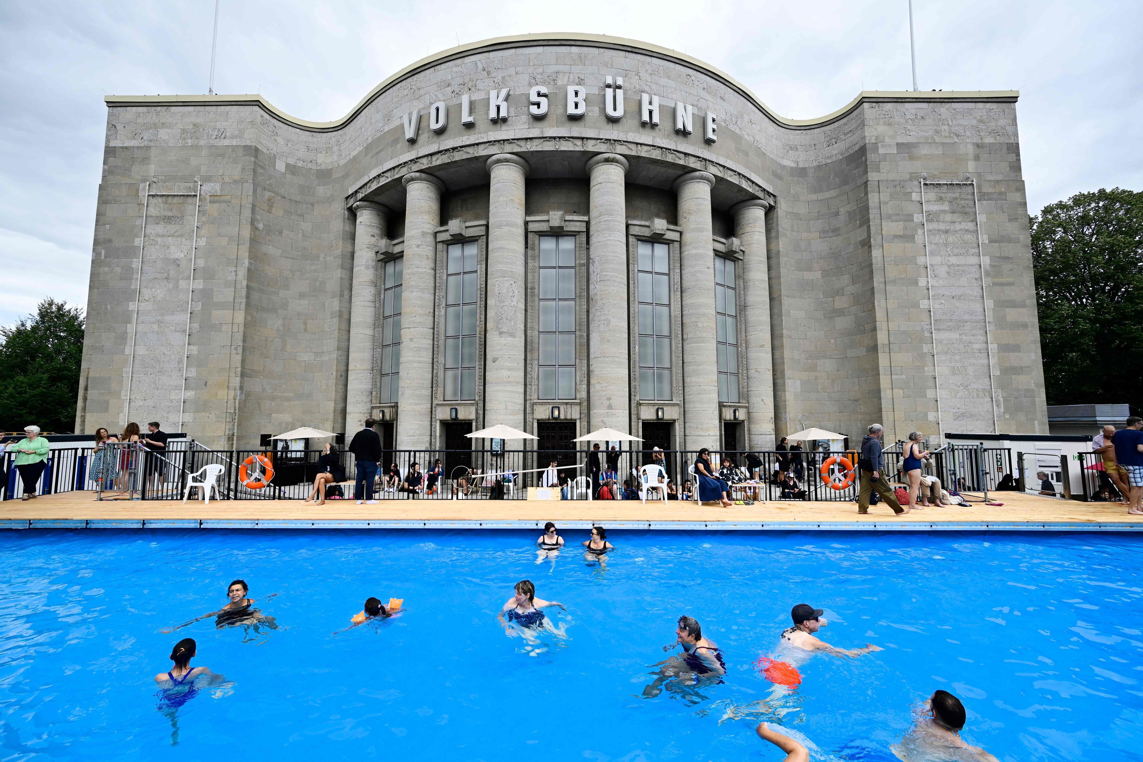 Vor einem Gebäude ist ein großer Pool aufgebaut, in dem Menschen schwimmen.