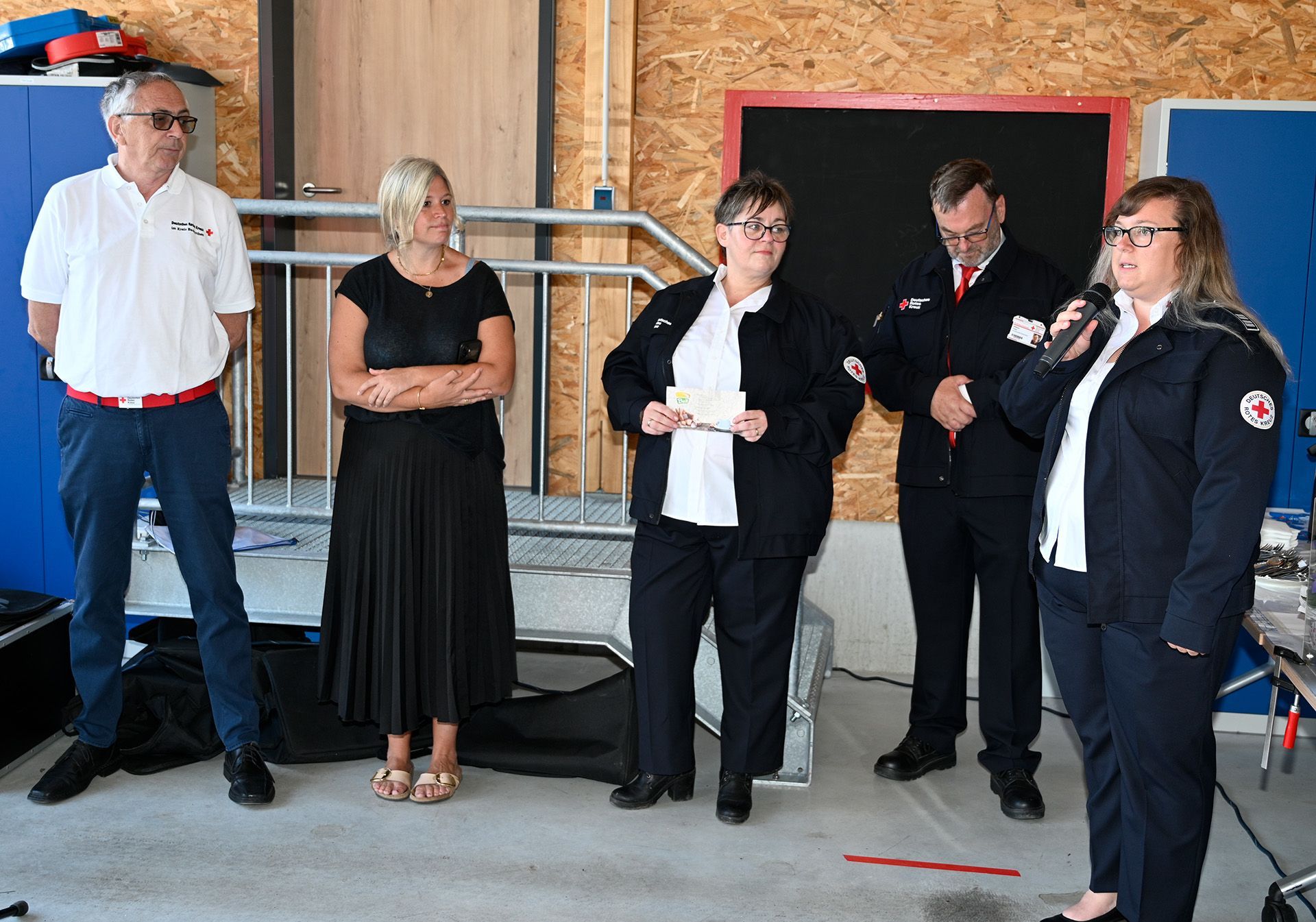Eine Frau in Rotkreuz-Weste spricht in ein Mikro, zwei Männer und zwei Frauen stehen neben ihr.