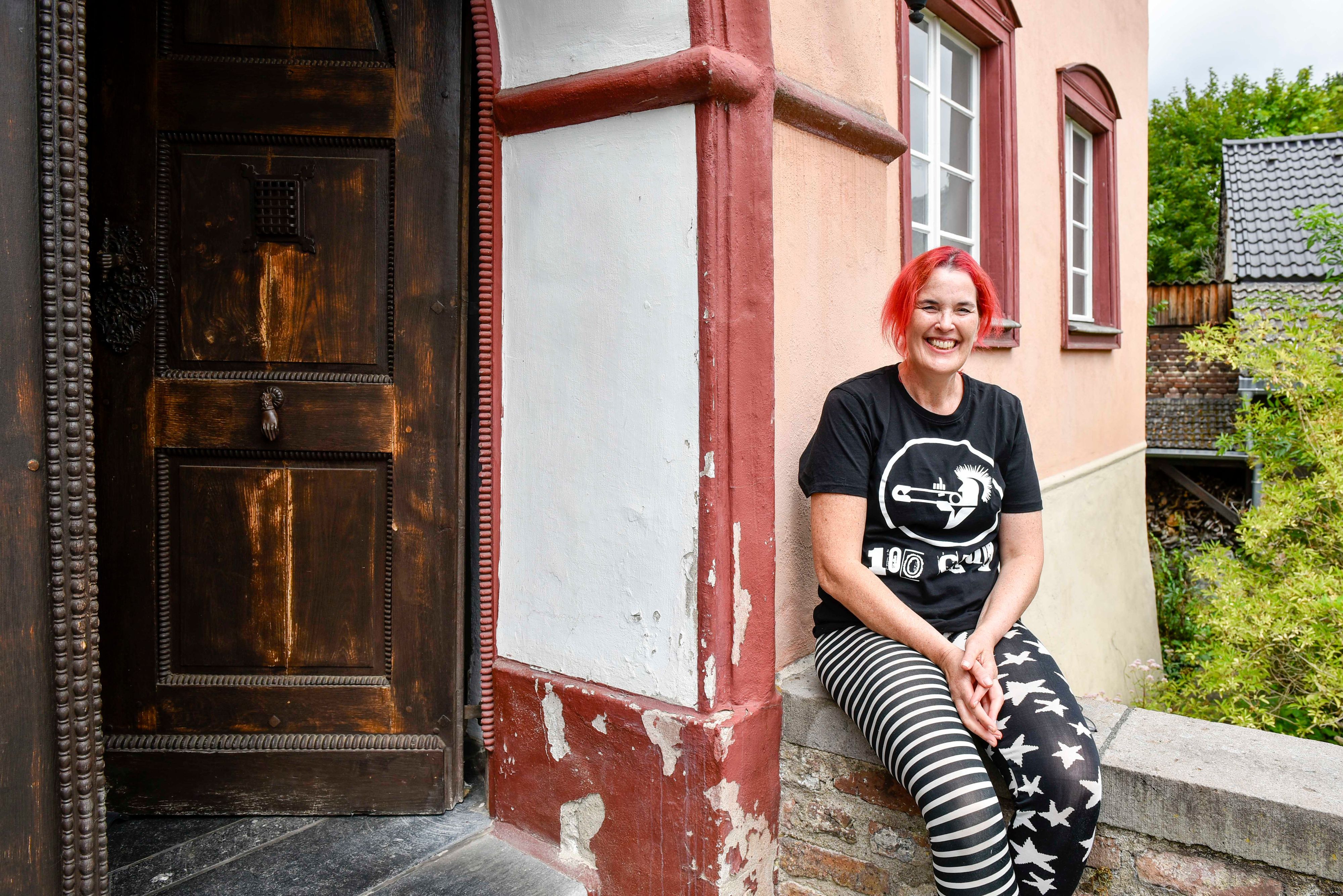 Eine Frau sitzt auf einer Mauer vor einem Haus.