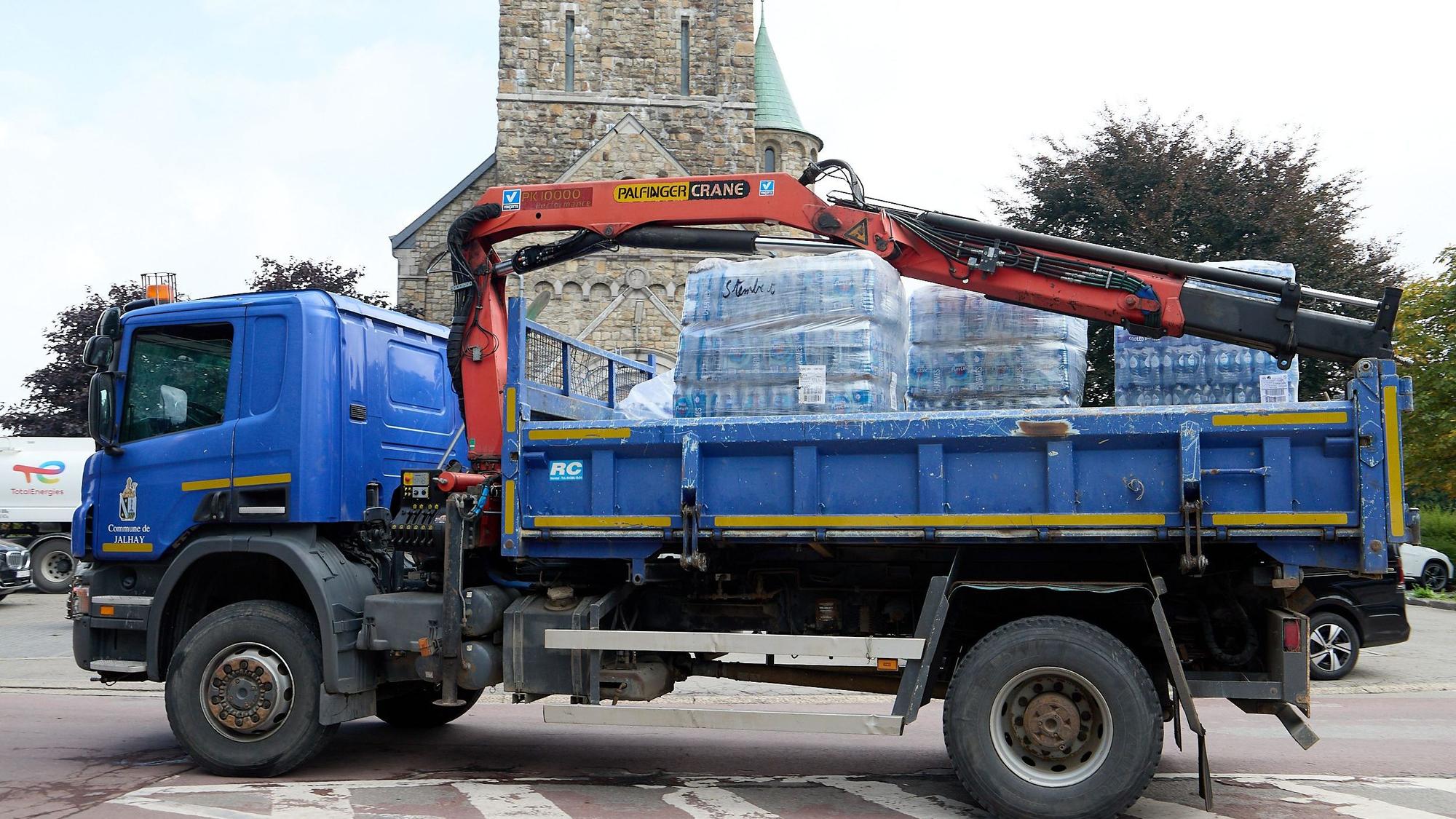 Auf einem blauen Lastwagen mit Ladekran befinden sich mehrere Paletten mit Wasserflaschen.