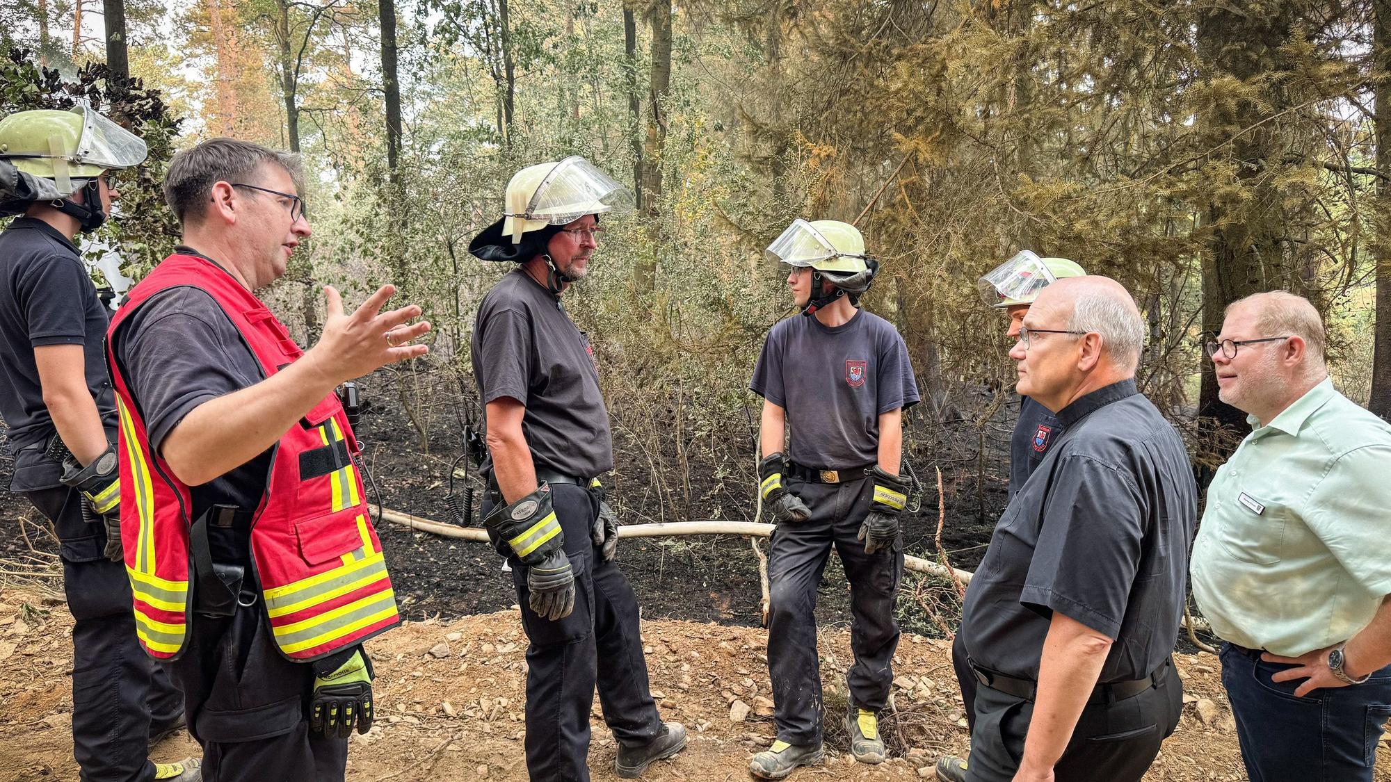 Helmut Dieser (2.v.r.), Bischof von Aachen, besucht Einsatzkräfte der Feuerwehr vor Ort in Hürtgenwald. Ralf Nolten (2.v.l.), Landrat des Kreises Düren, und Stephan Cranen (r.), Bürgermeister von Hürtgenwald, informieren ihn über den aktuellen Waldbrand in der Eifel.