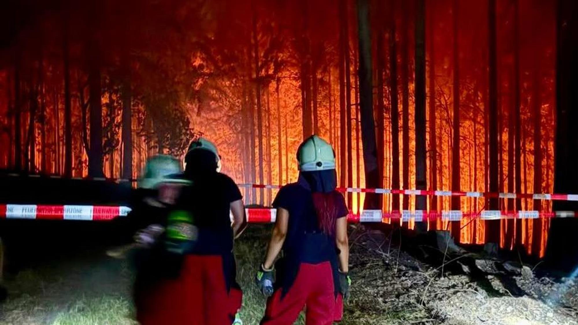 Einsatzkräfte der Feuerwehr stehen vor einer Polizeiabsperrung im Hürtgenwald.