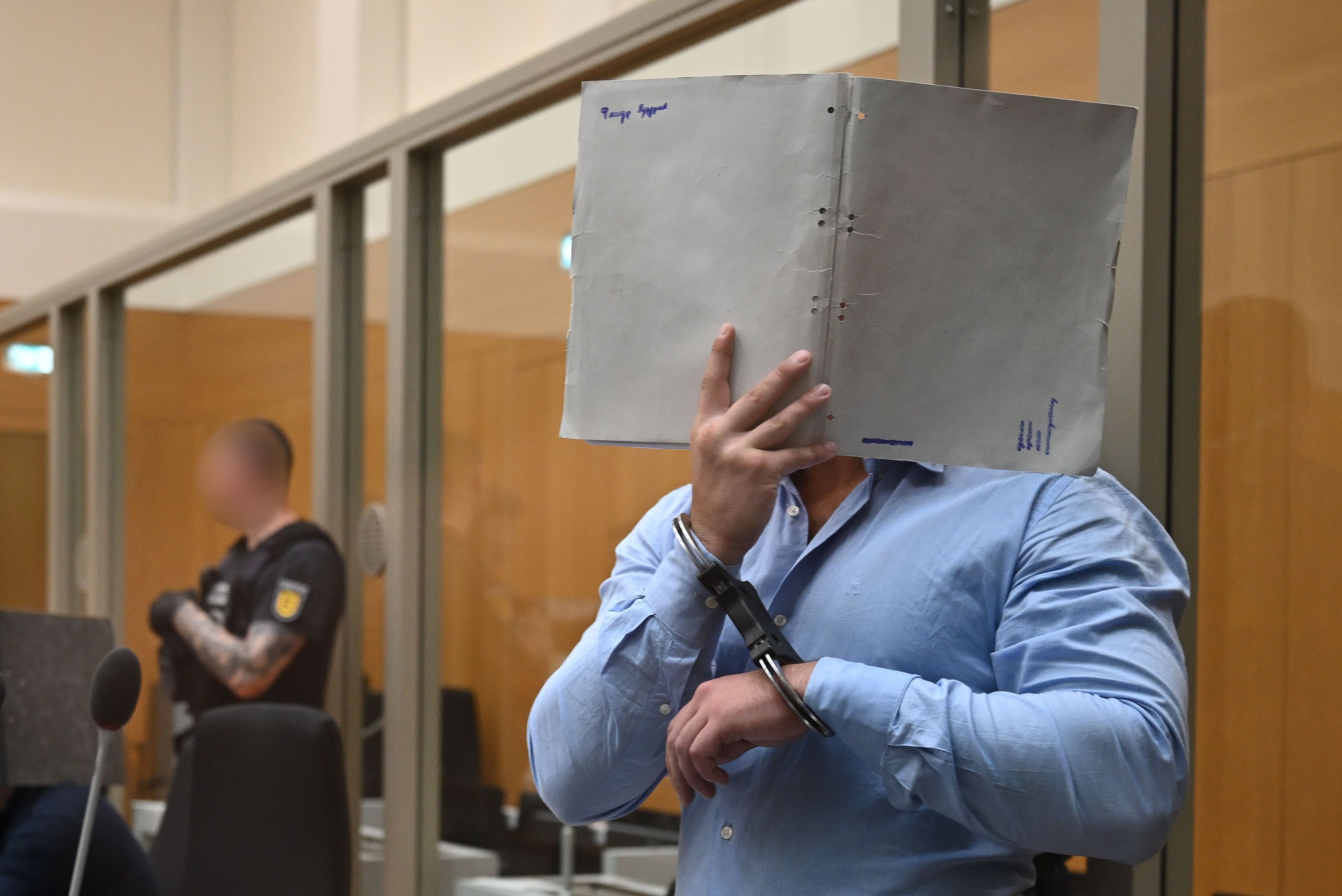 Einer der Angeklagten in einem Staatsschutzverfahren gegen drei Ukrainer wegen Agententätigkeit im Auftrag eines russischen Nachrichtendienstes kommt in Handschellen in den Saal des Oberlandesgerichts Stuttgart in Stammheim und verdeckt sein Gesicht mit einem Aktenordner.