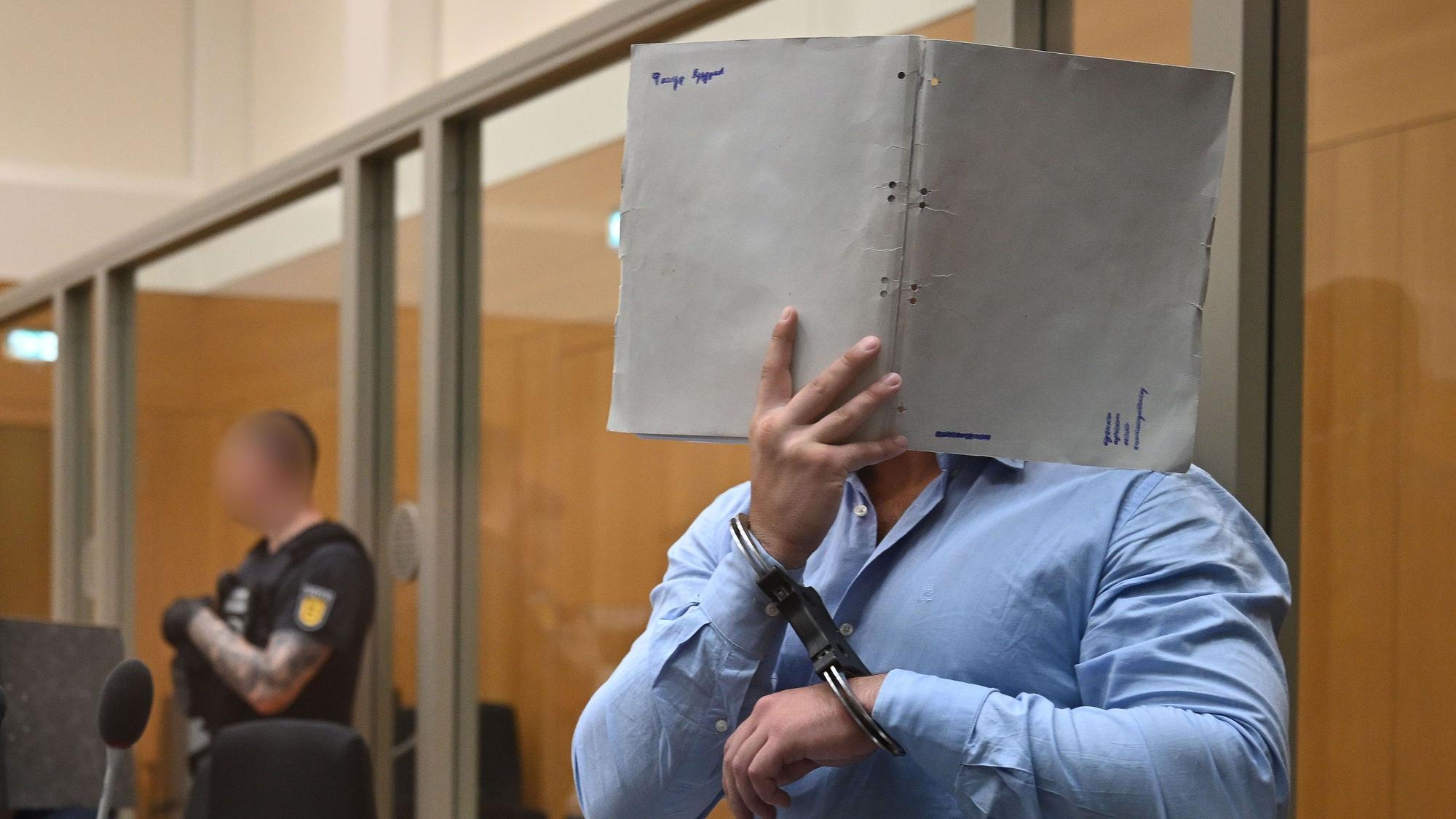 Einer der Angeklagten in einem Staatsschutzverfahren gegen drei Ukrainer wegen Agententätigkeit im Auftrag eines russischen Nachrichtendienstes kommt in Handschellen in den Saal des Oberlandesgerichts Stuttgart in Stammheim und verdeckt sein Gesicht mit einem Aktenordner.