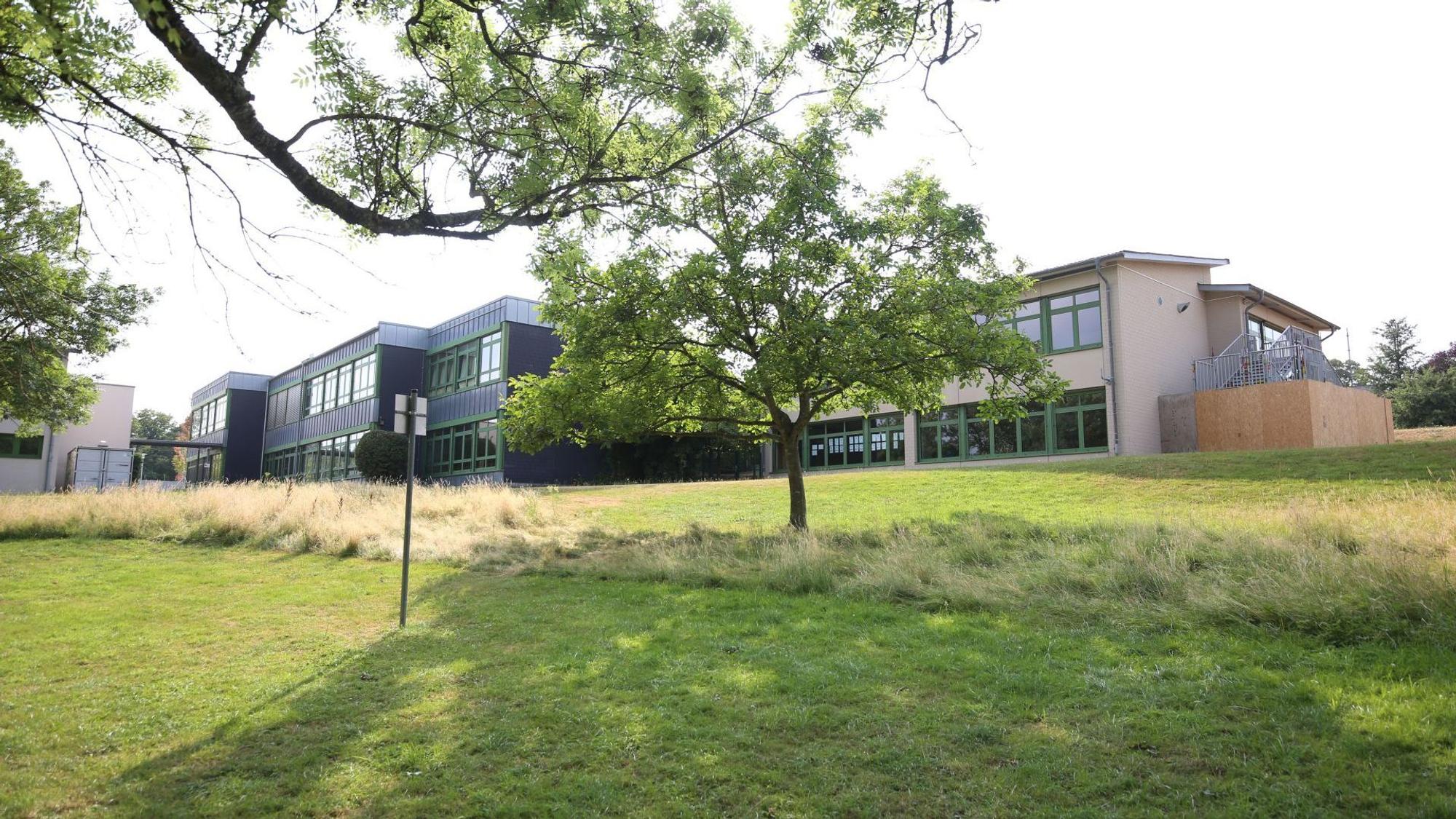 Mehrere zweigeschossige Gebäude, im Vordergrund eine Wiese und ein Baum.