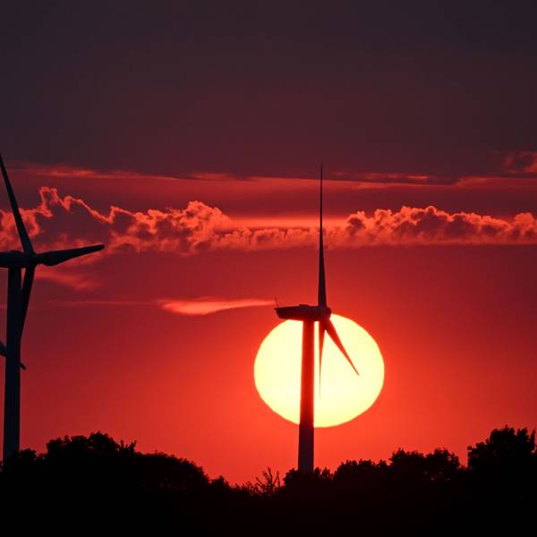 Hinter Windrädern färbt die sinkende Sonne den Himmel rot.