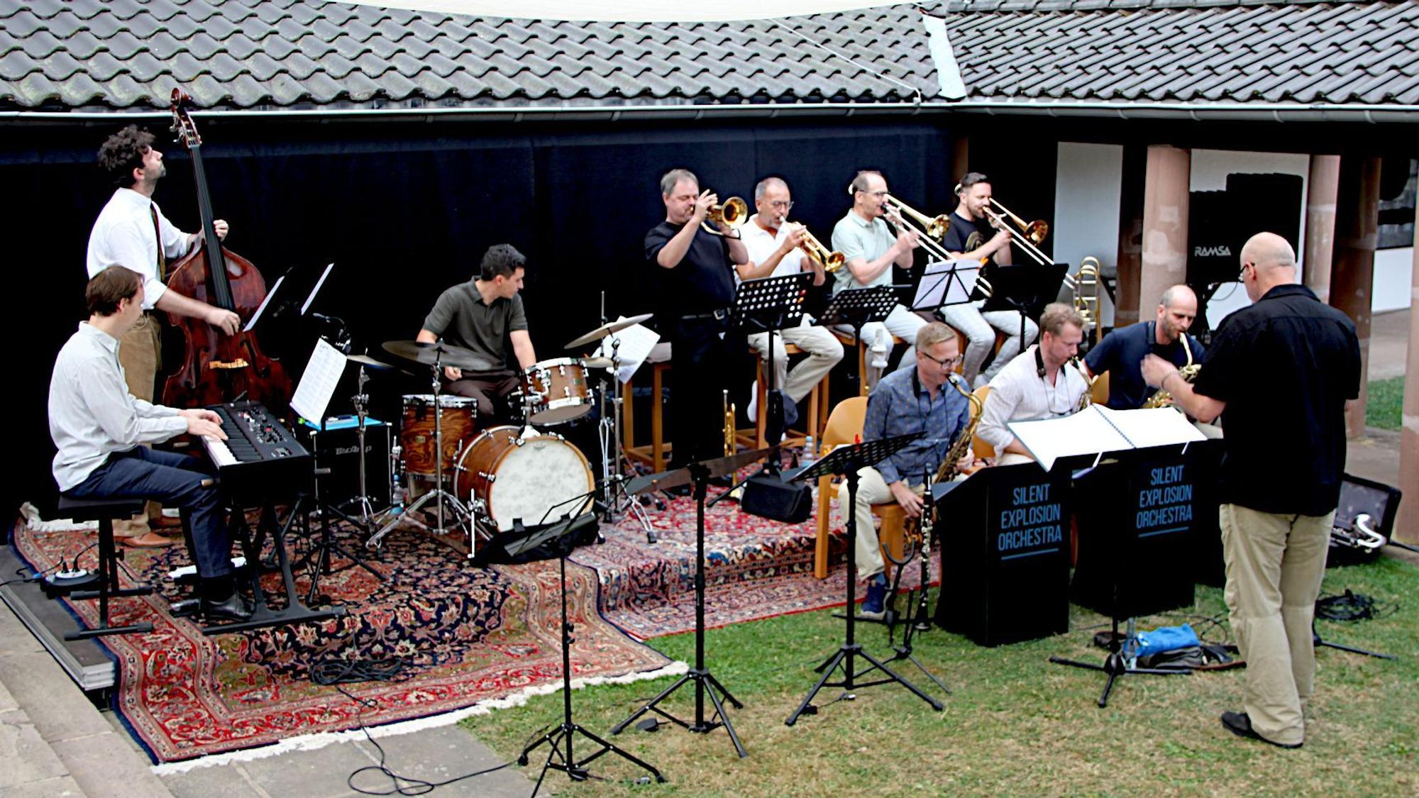 Eine Band mit zehn Musikern spielt auf einer improvisierten Bühne.