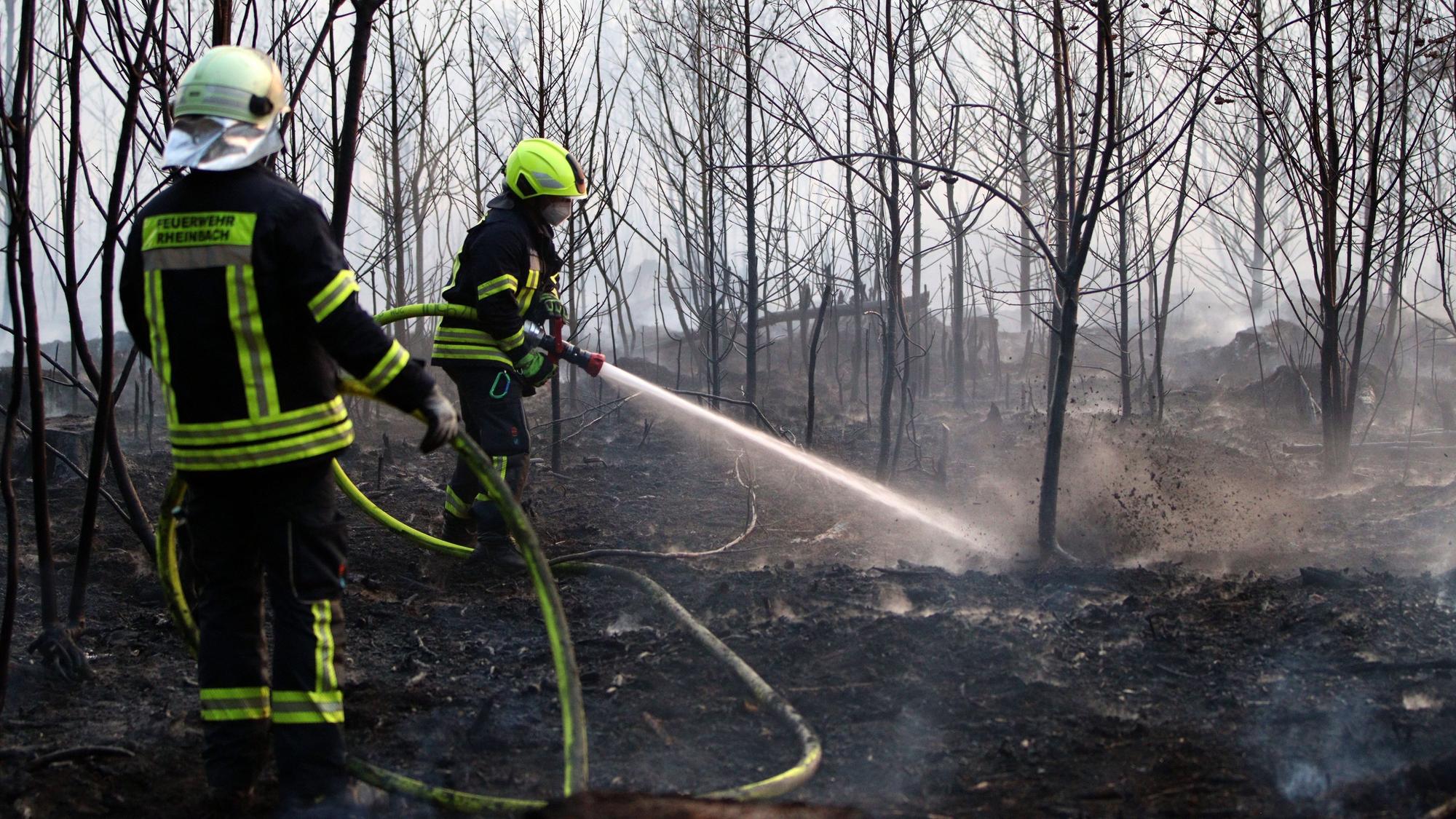 Zwei Feuerwehrleute löschen mit Wasser aus einem Hohlstrahlrohr den Brand im Wald bei Flamersheim.