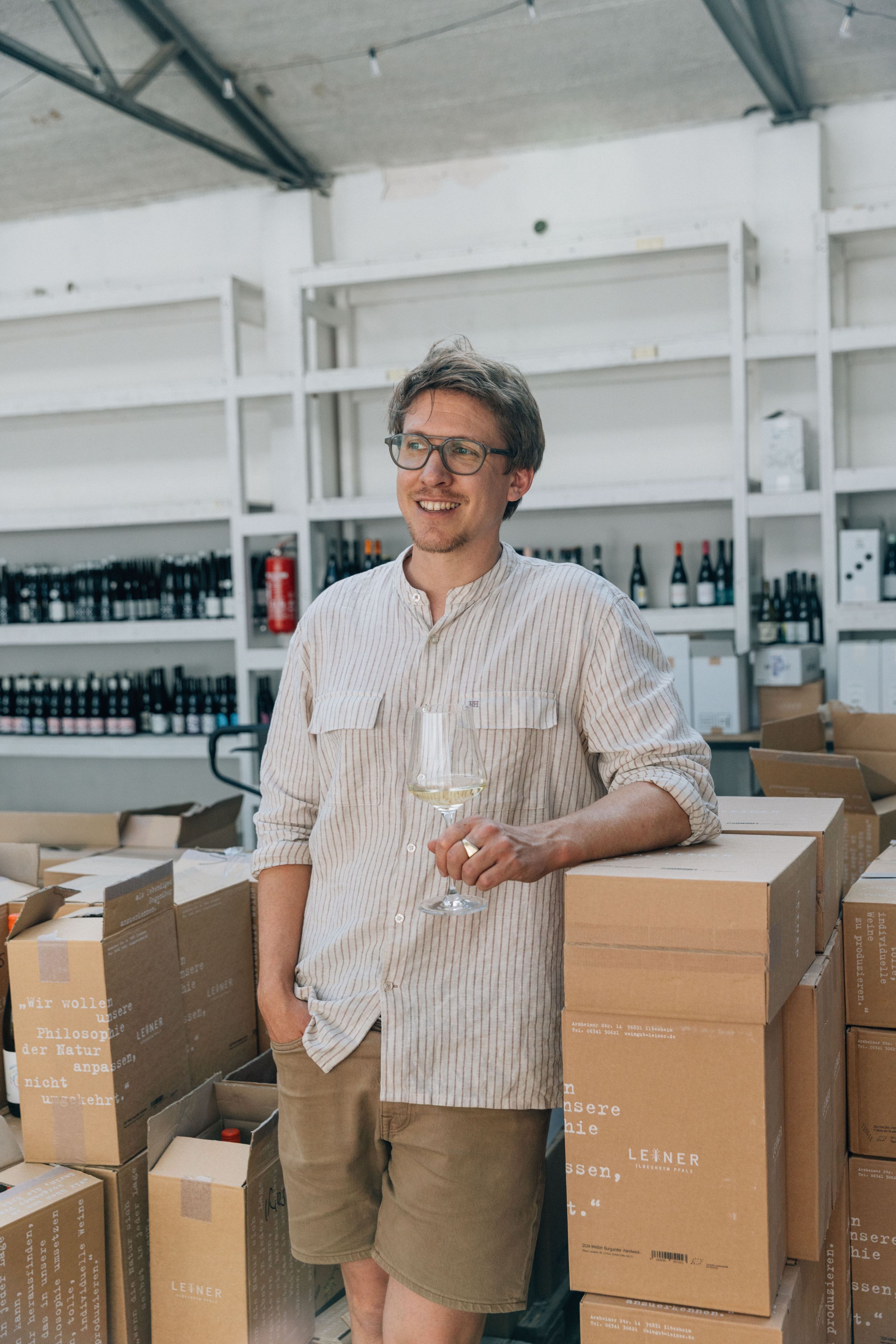 Fabian Lay steht mit einem Weinglas in der Hand vor einem Weinregal.