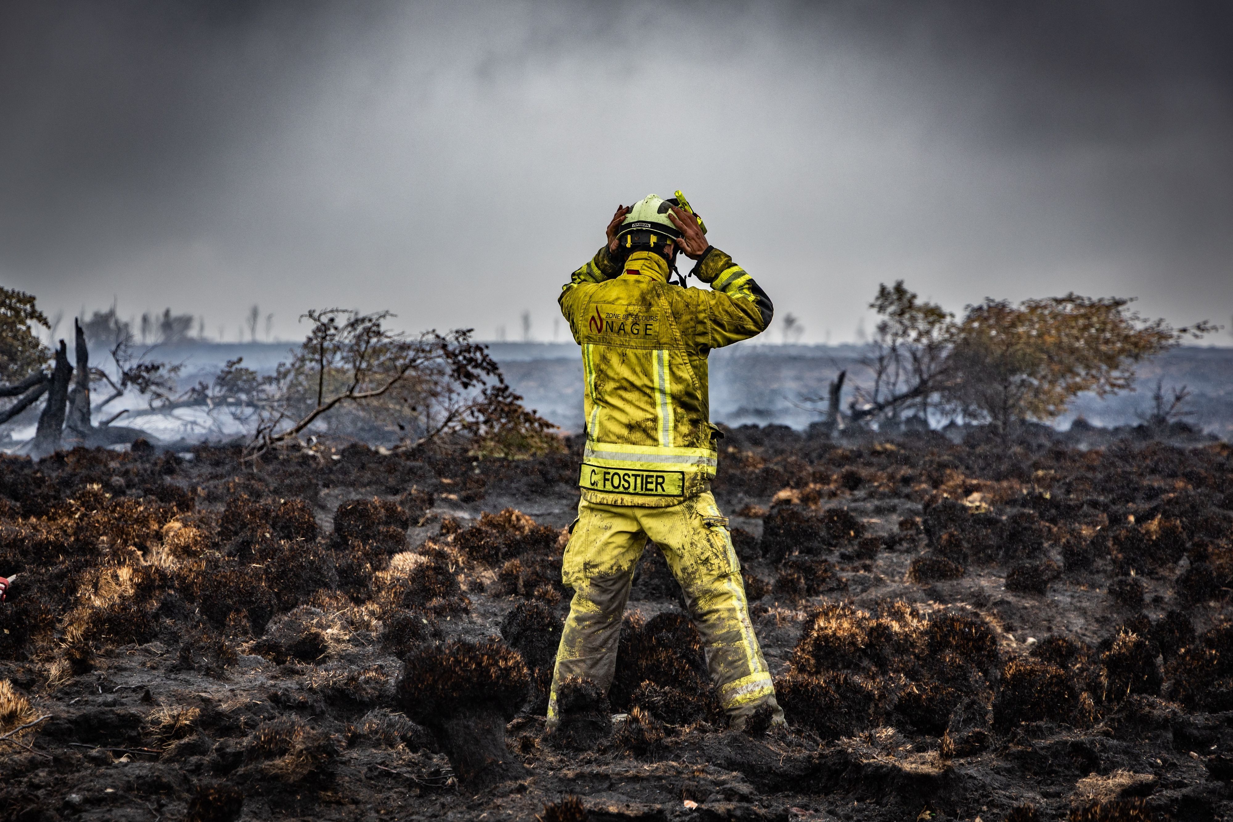 Ein Feuerwehrmann steht auf der verkohlten Erde eines Waldbrandes.