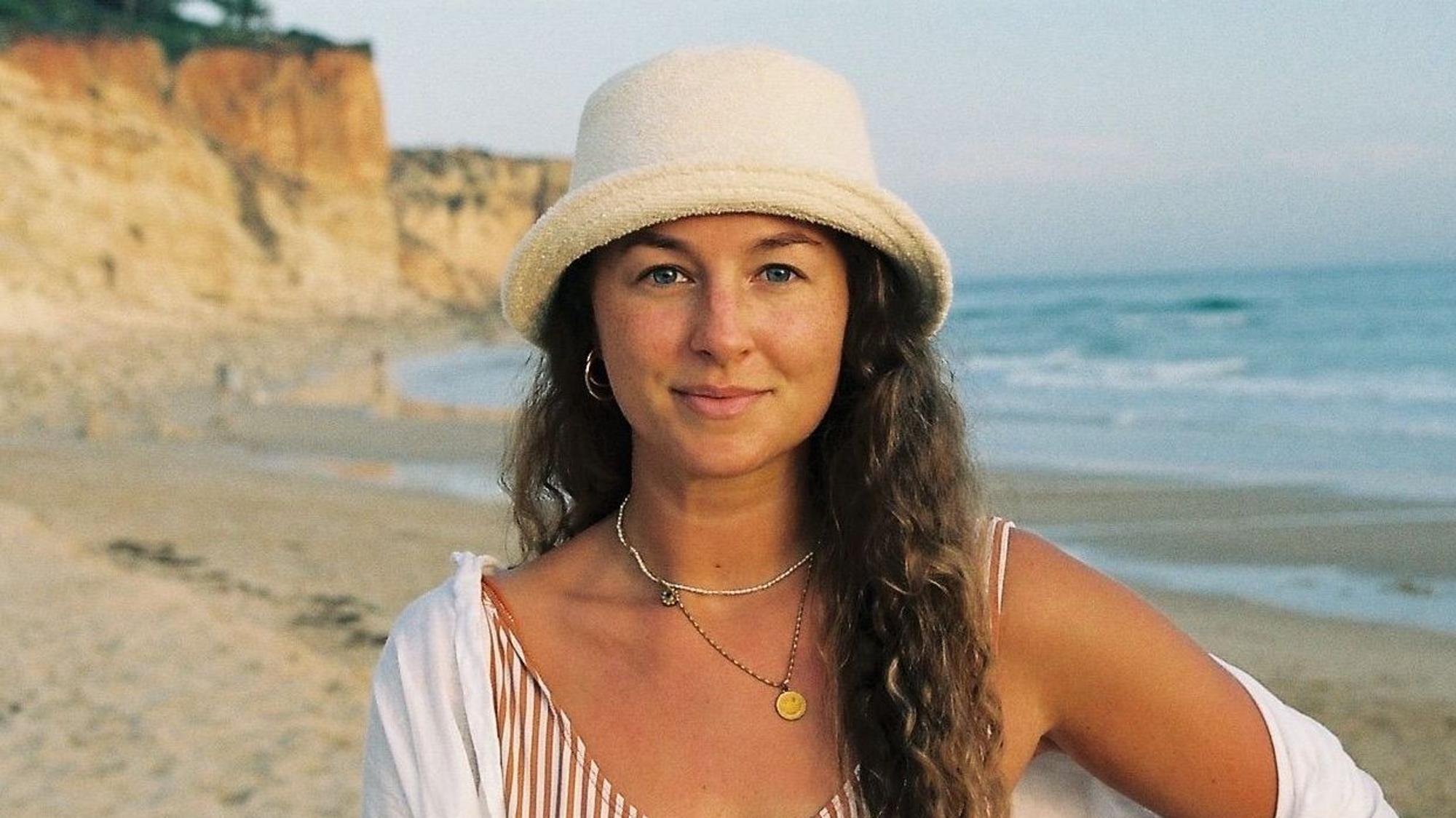 Eine Frau steht am Strand und lächelt in die Kamera.
