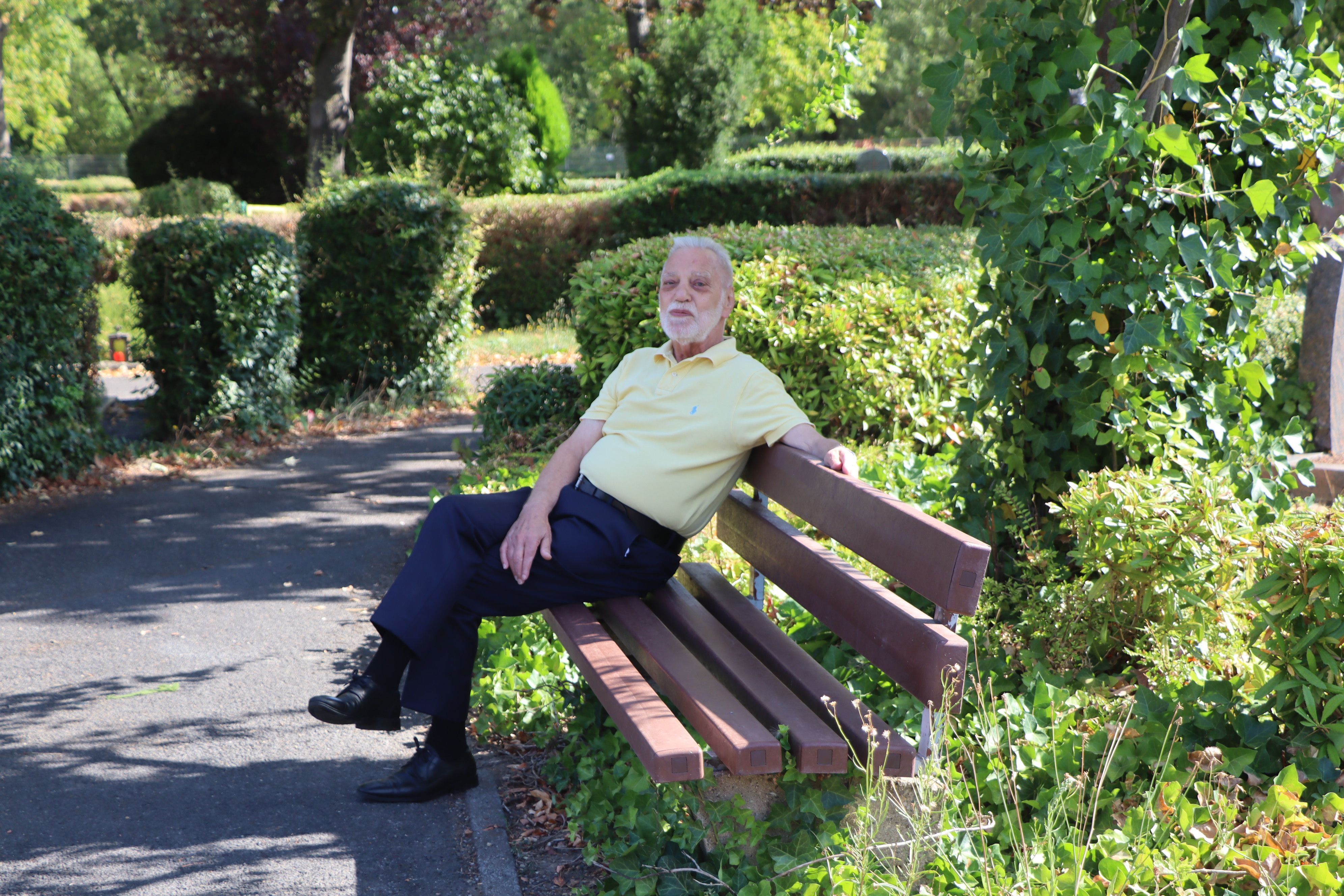 Ein Mann sitzt auf einer Bank auf einem Friedhof.
