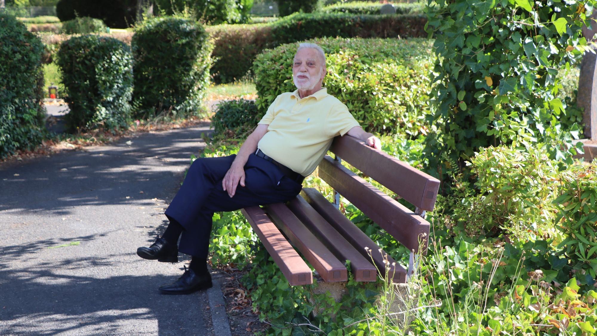 Ein Mann sitzt auf einer Bank auf einem Friedhof.