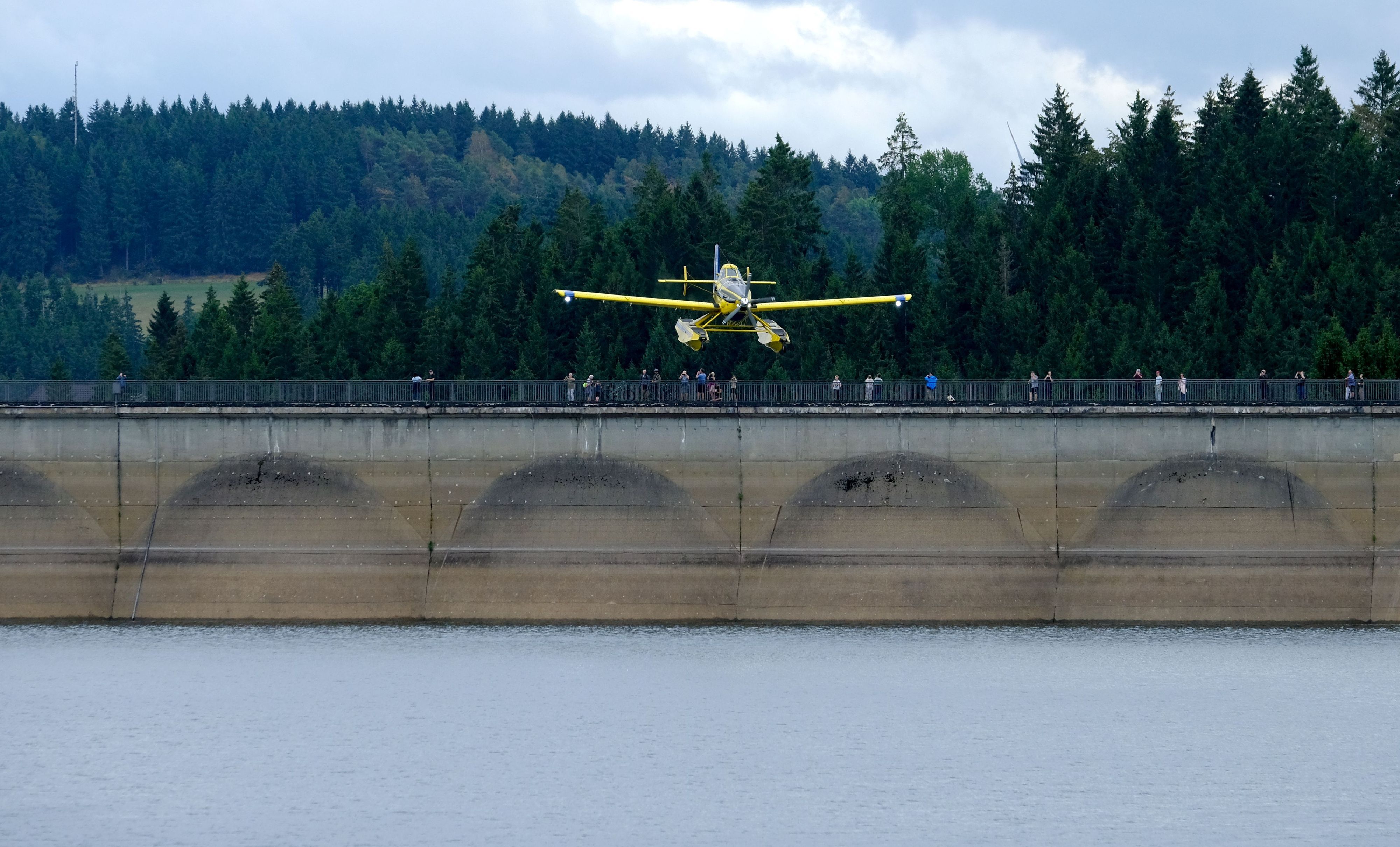 Von der Dammkrone aus beobachten zahlreiche Schaulustige den Anflug eines gelben Löschflugzeugs an der Oleftalsperre.