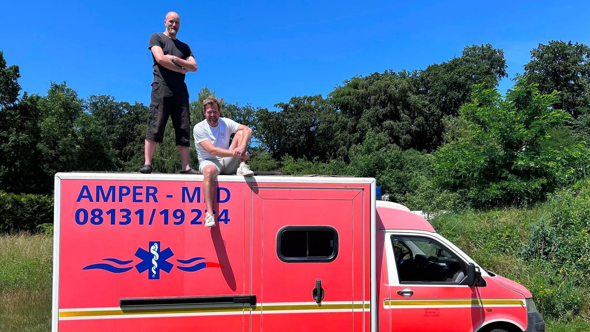 Ein roter Rettungswagen ein Mann sitzt auf dem Dach, ein anderer steht darauf