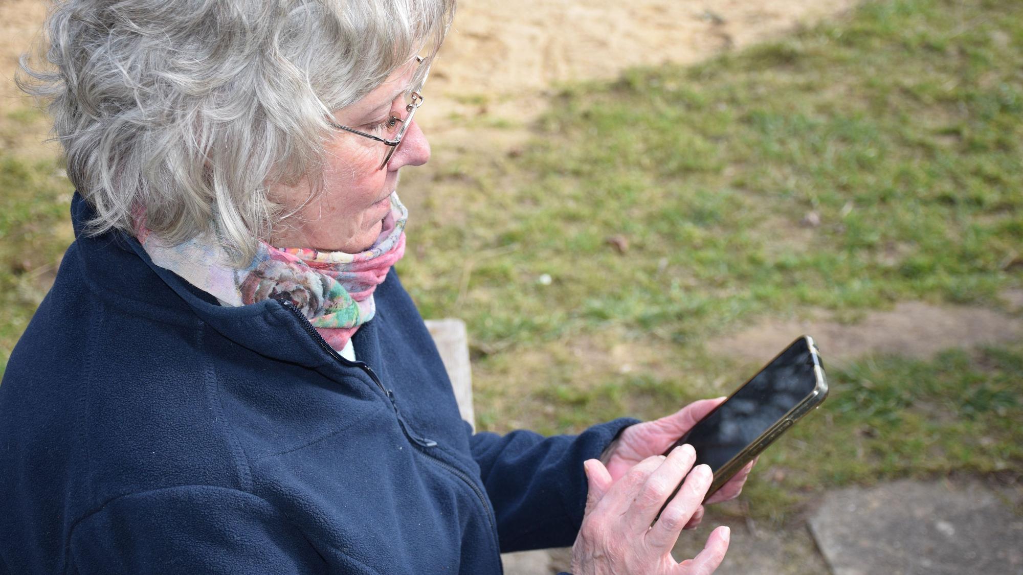 Eine Frau mit grauen Haaren hält ein Smartphone in der Hand und tippt auf dem Bildschirm.