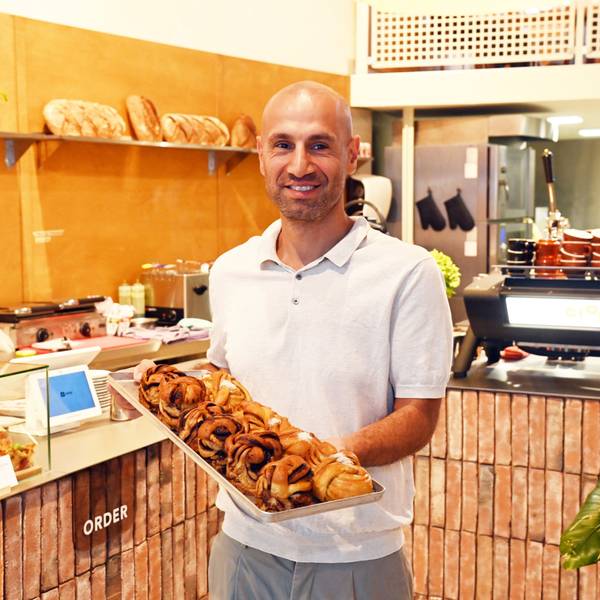 Rafet Aydogdu steht vor seiner Ladentheke und hält ein Blech mit Backwaren in die Kamera.