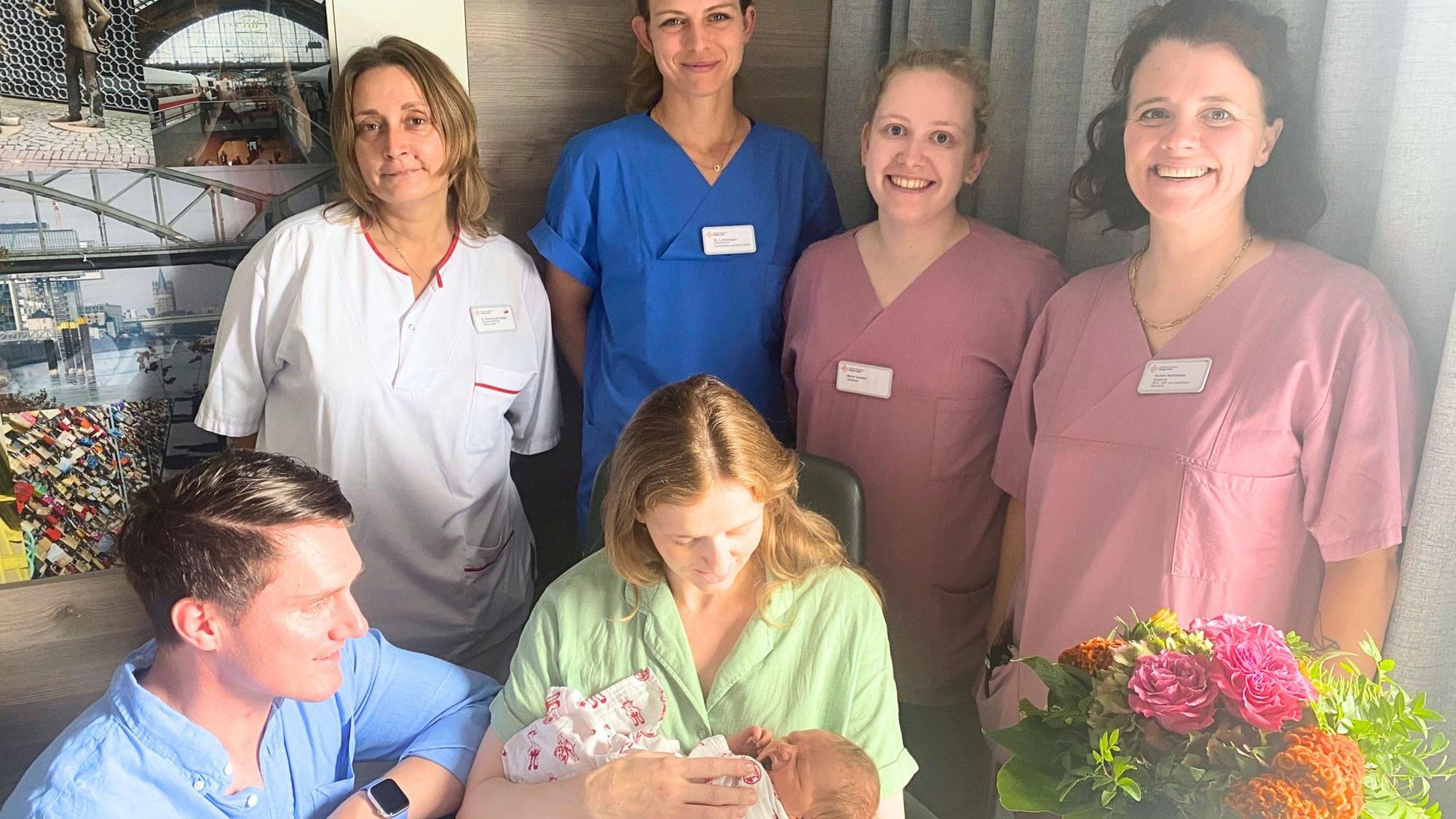 Baby Louis liegt in den Armen seiner Mutter. Daneben sind sein Vater sowie vier Mitarbeiter der Klinik zu sehen.