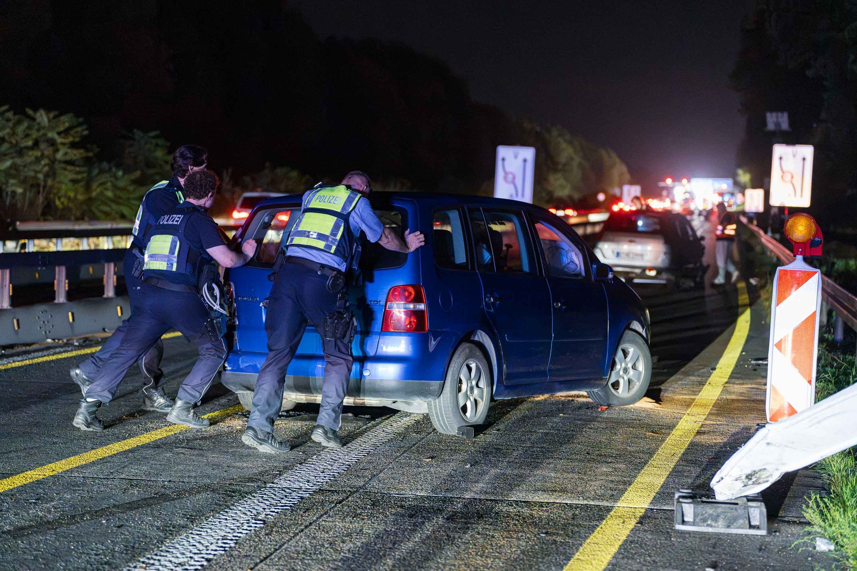 Polizisten schieben den verunfallten Wagen auf einer Autobahn.