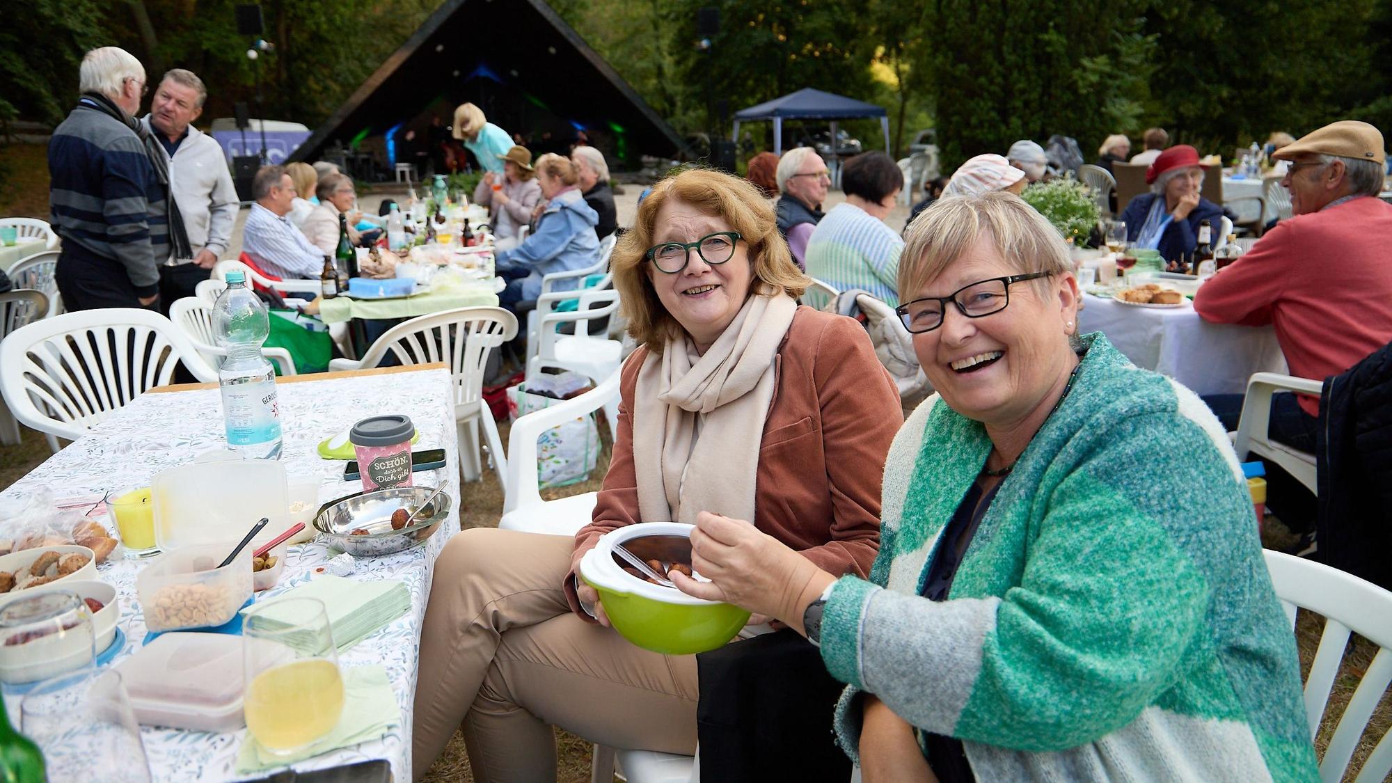 Die beiden Frauen sitzen an einem gedeckten Picknicktisch inmitten anderer Besucher.