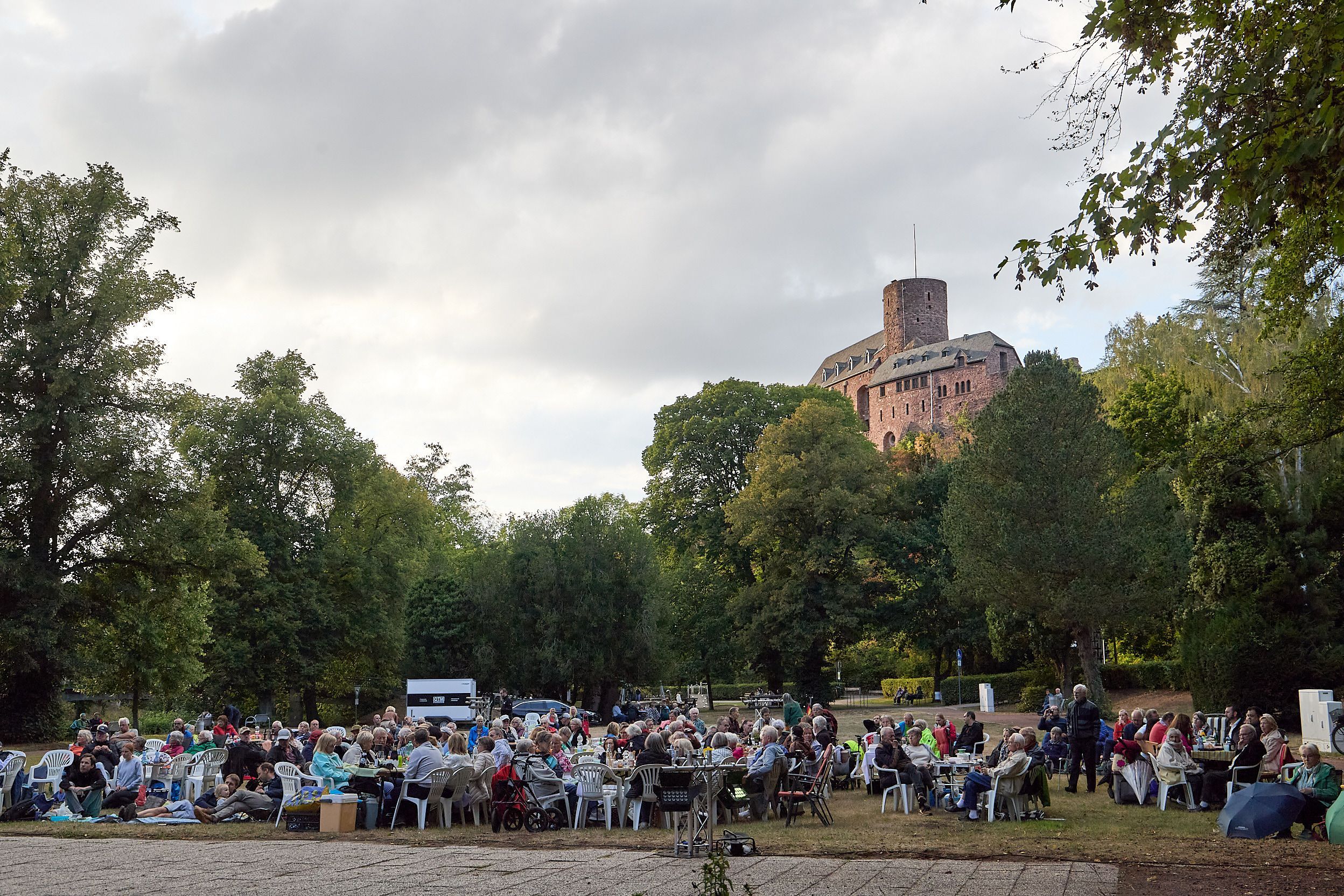 In Vordergrund sitzen die Besucher des Picknickkonzerts, im Hintergrund ragt die Burg Hengebach über ihnen.