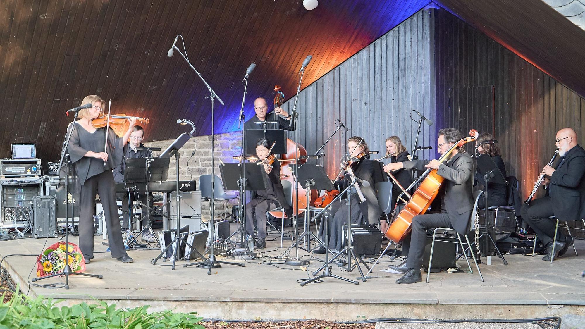 Das Orchester steht und sitzt auf einer Bühne.