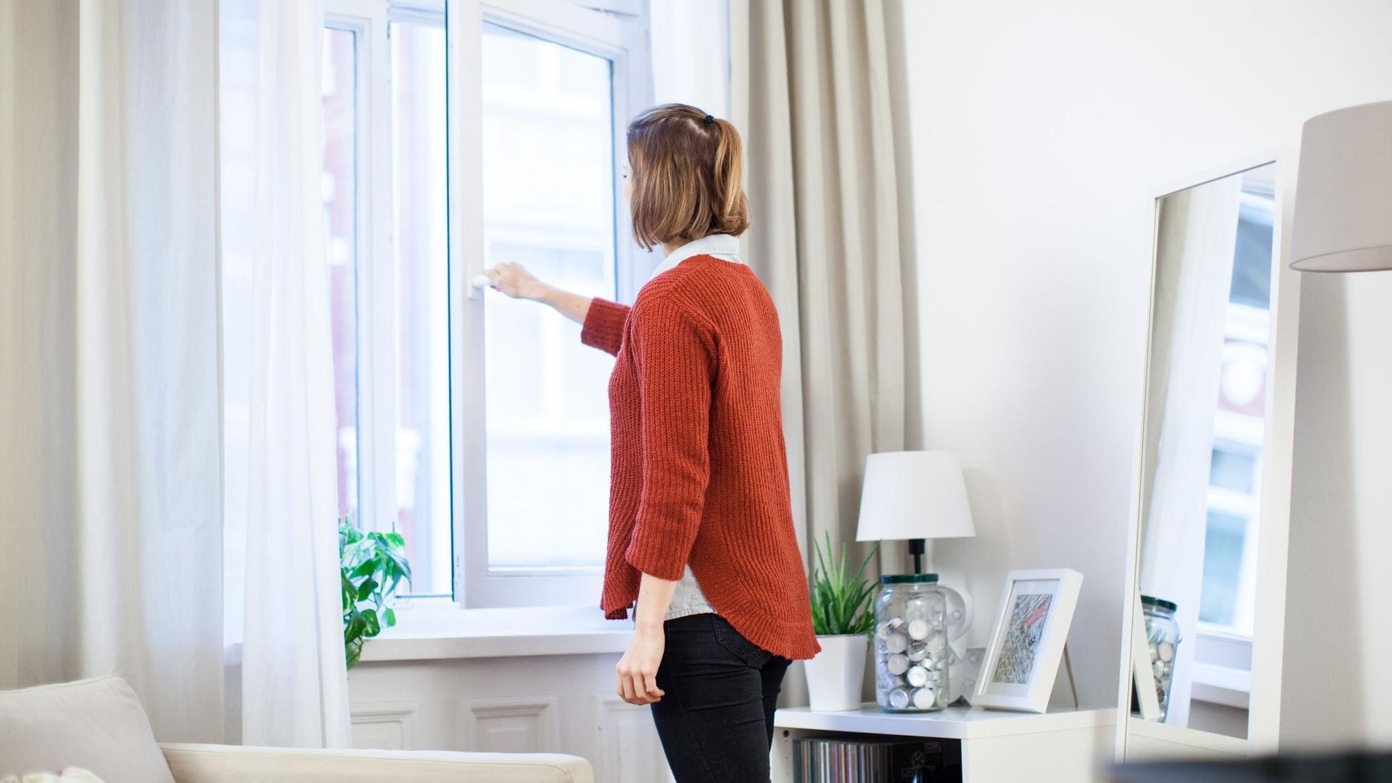Eine junge Frau öffnet in einer Wohnung das Fenster