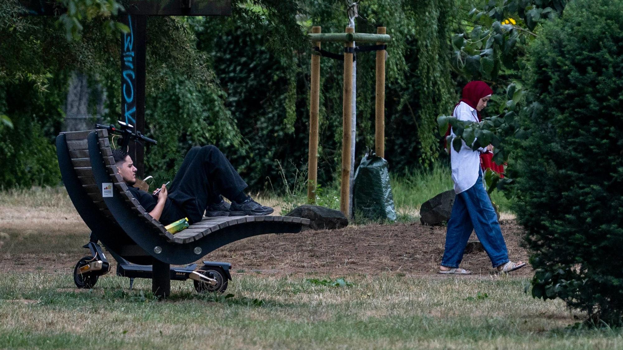 Ein junger Mann sitzt auf einer Holzliege.
