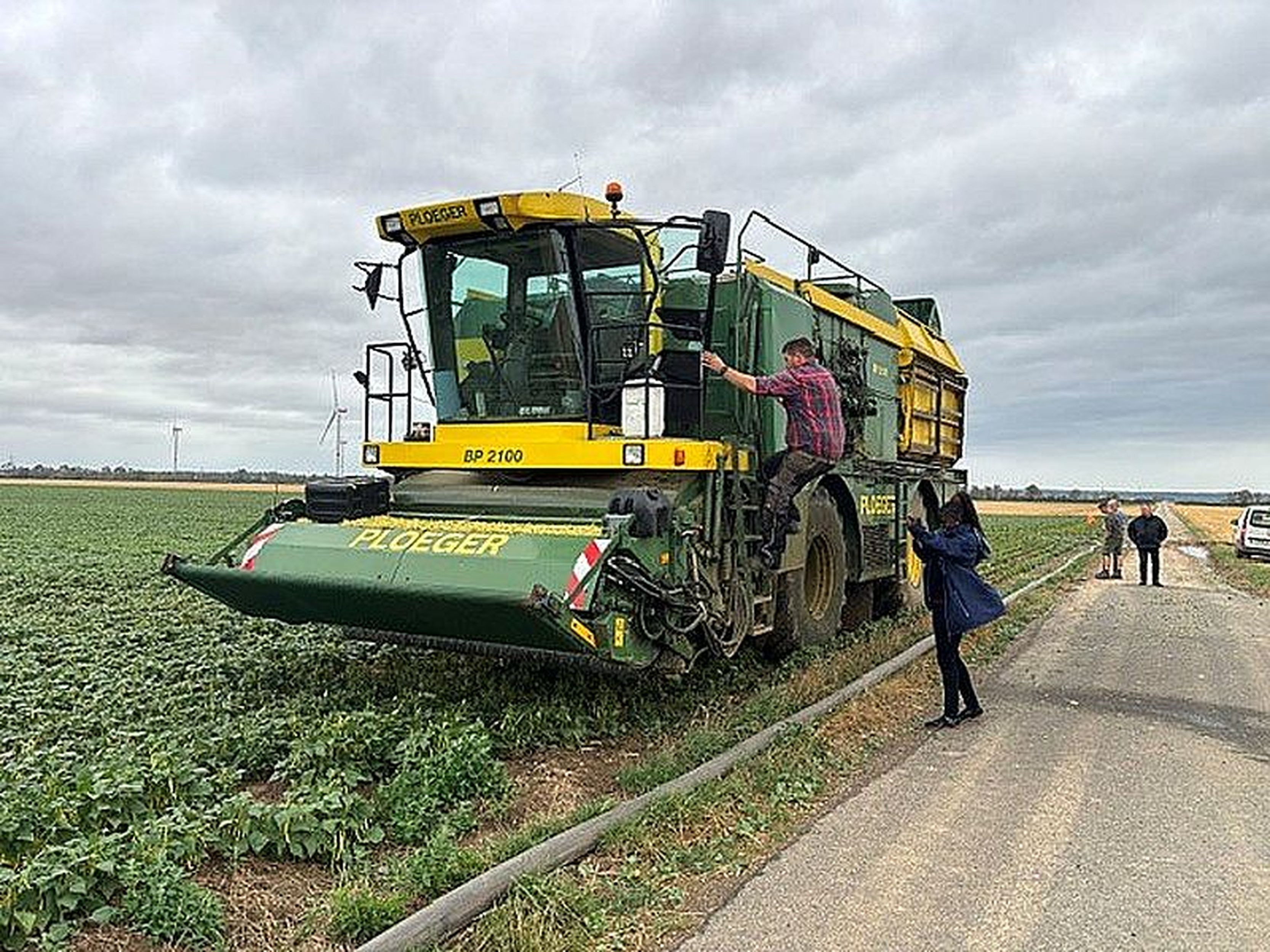 Bridgit Obuya steht auf einem Feldweg neben einer Erntemaschine, auf die gerade ein Mann steigt.